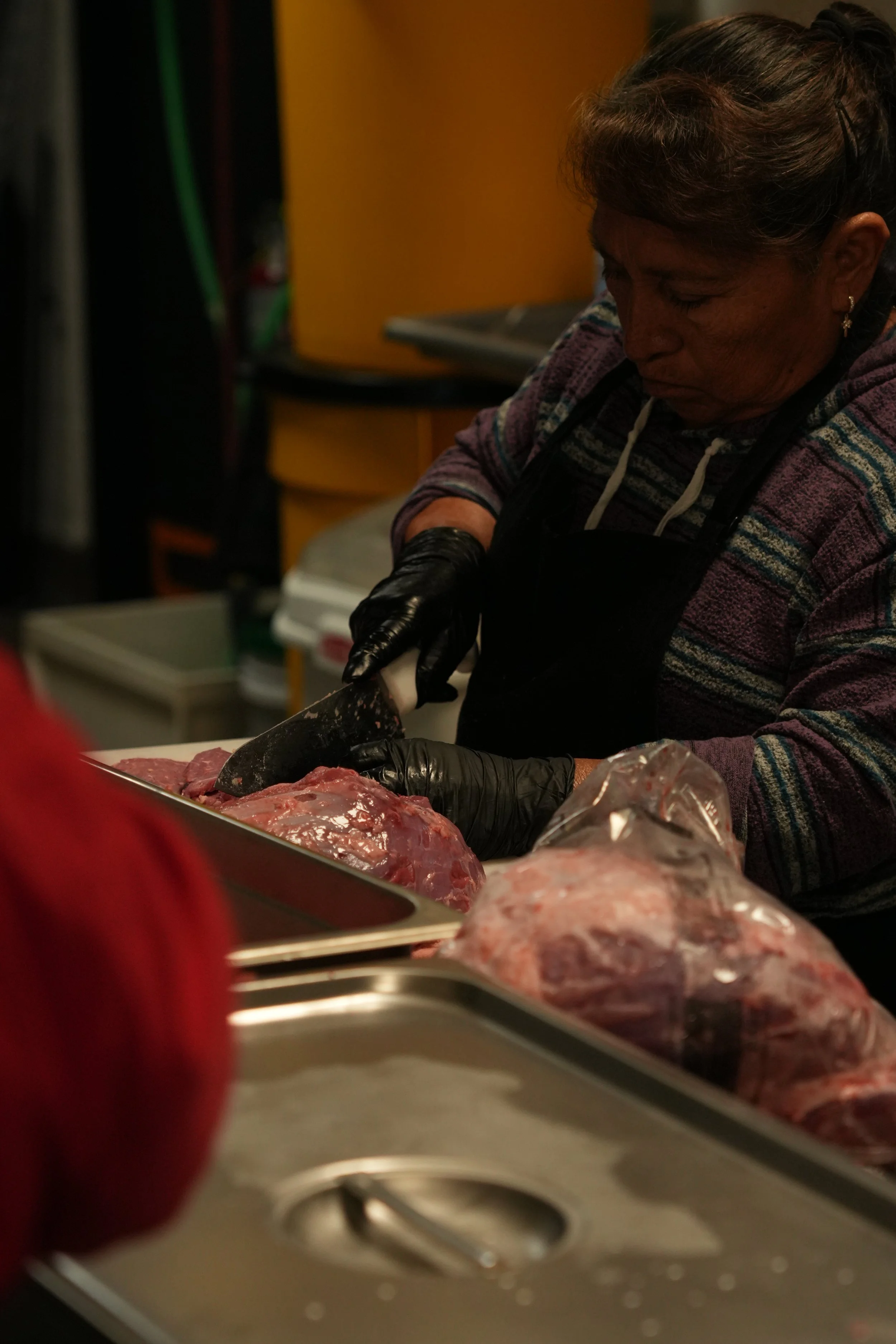 A woman wearing black gloves butchering raw meat in a kitchen setting.