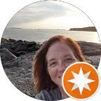 Partial view of a woman outdoors near the ocean at sunset, with rocks in the background.