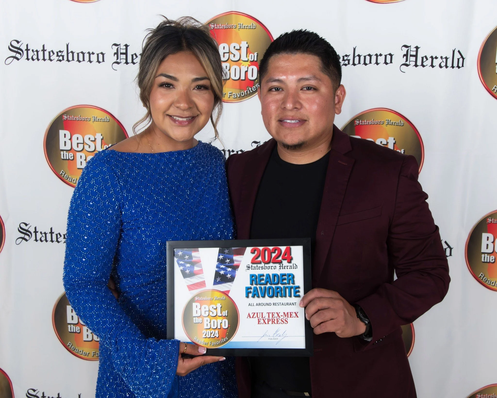 A woman in a sparkling blue dress and a man in a burgundy blazer are smiling and holding a certificate that says '2024 Best of the Boro' with a logo mentioning 'Reader Favorite' at the 'Statesboro Herald' awards event.