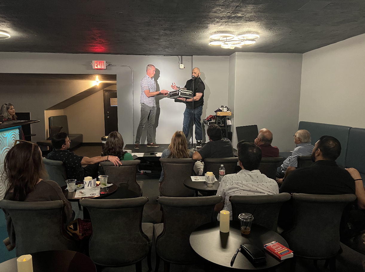 People watching a presentation or award ceremony in a dark room, with one person on stage handing a tray to another.