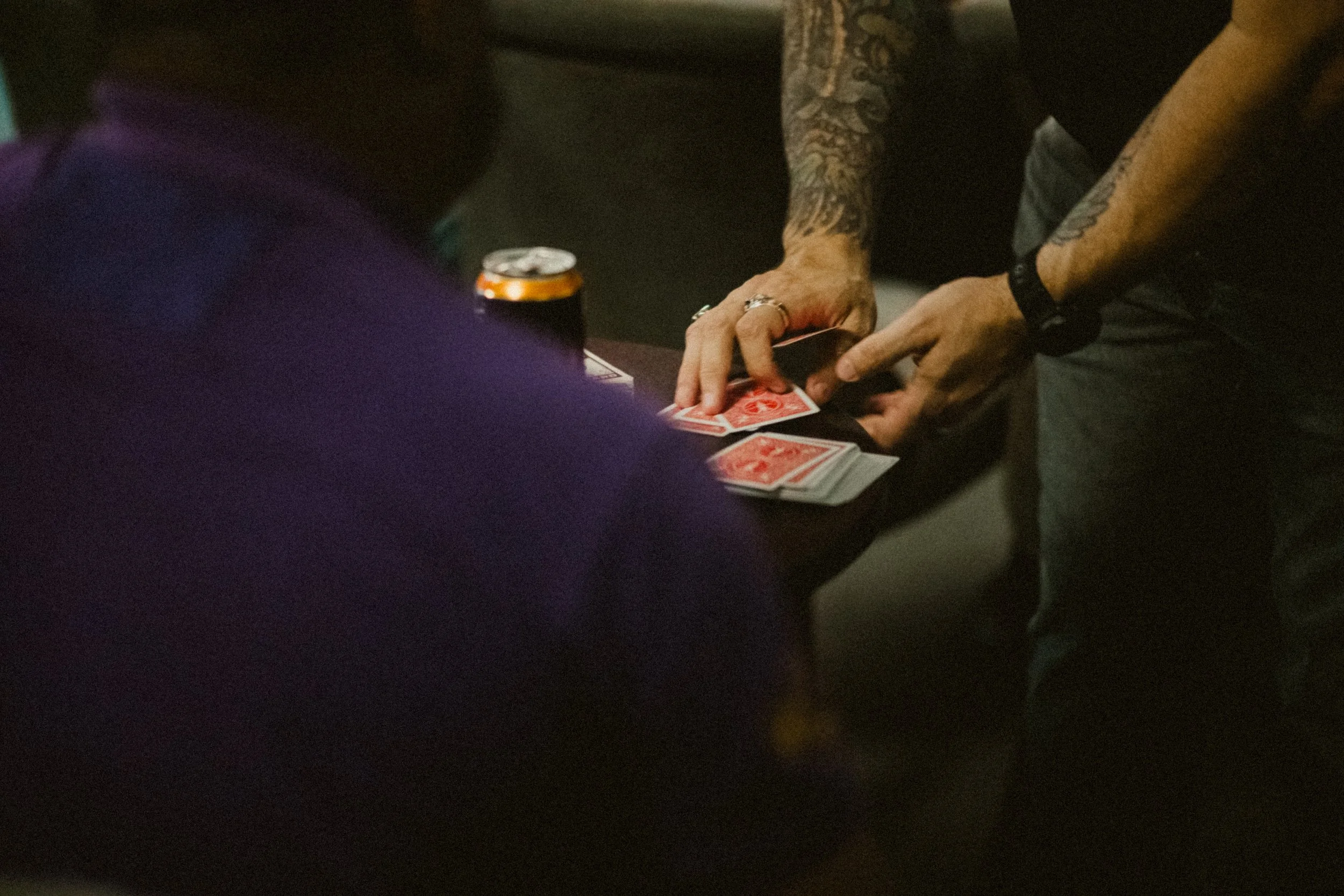 People playing a card game at a table, with a can of drink on the surface.