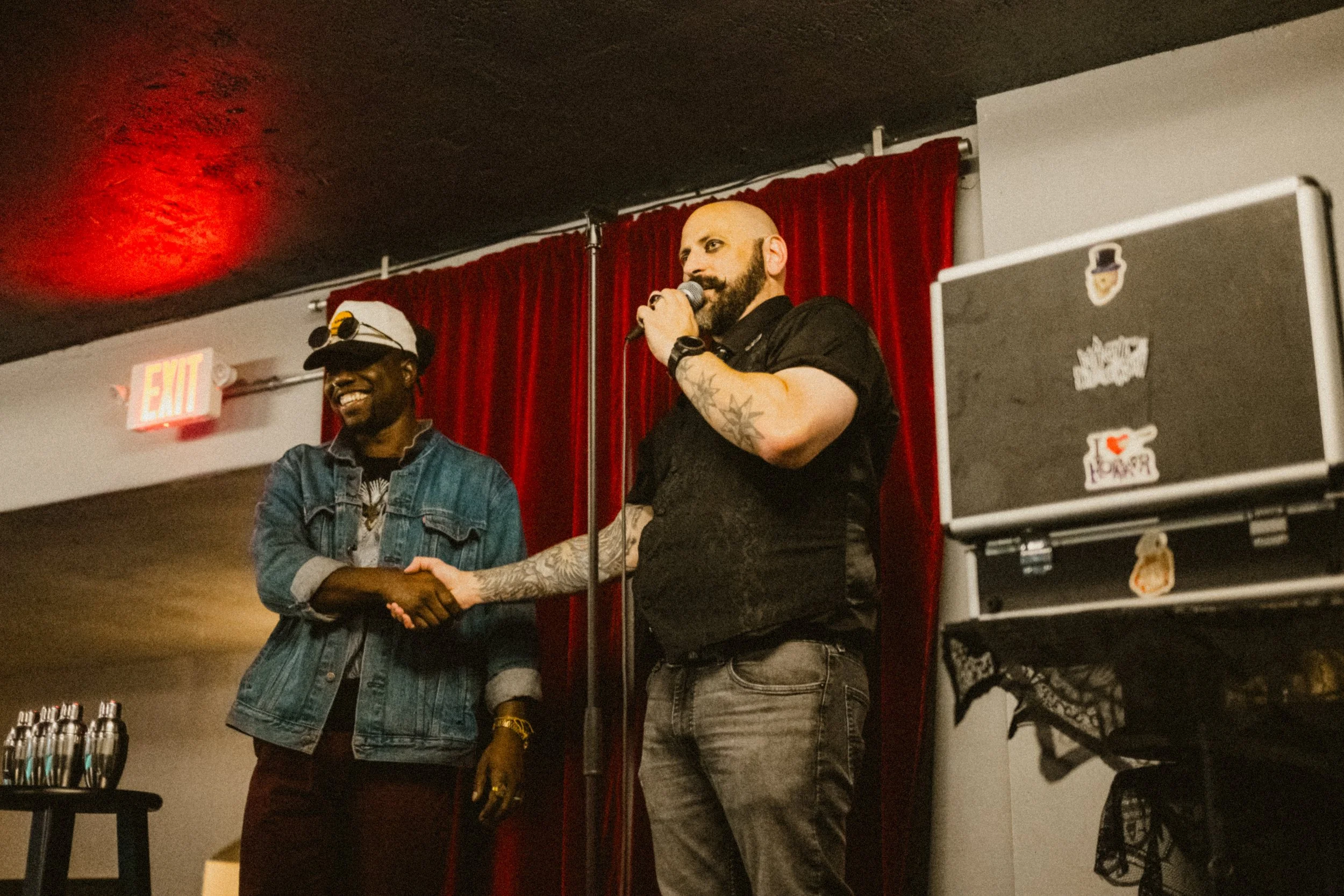 Magician and an audience member shaking hands on a stage, with red curtains in the background.