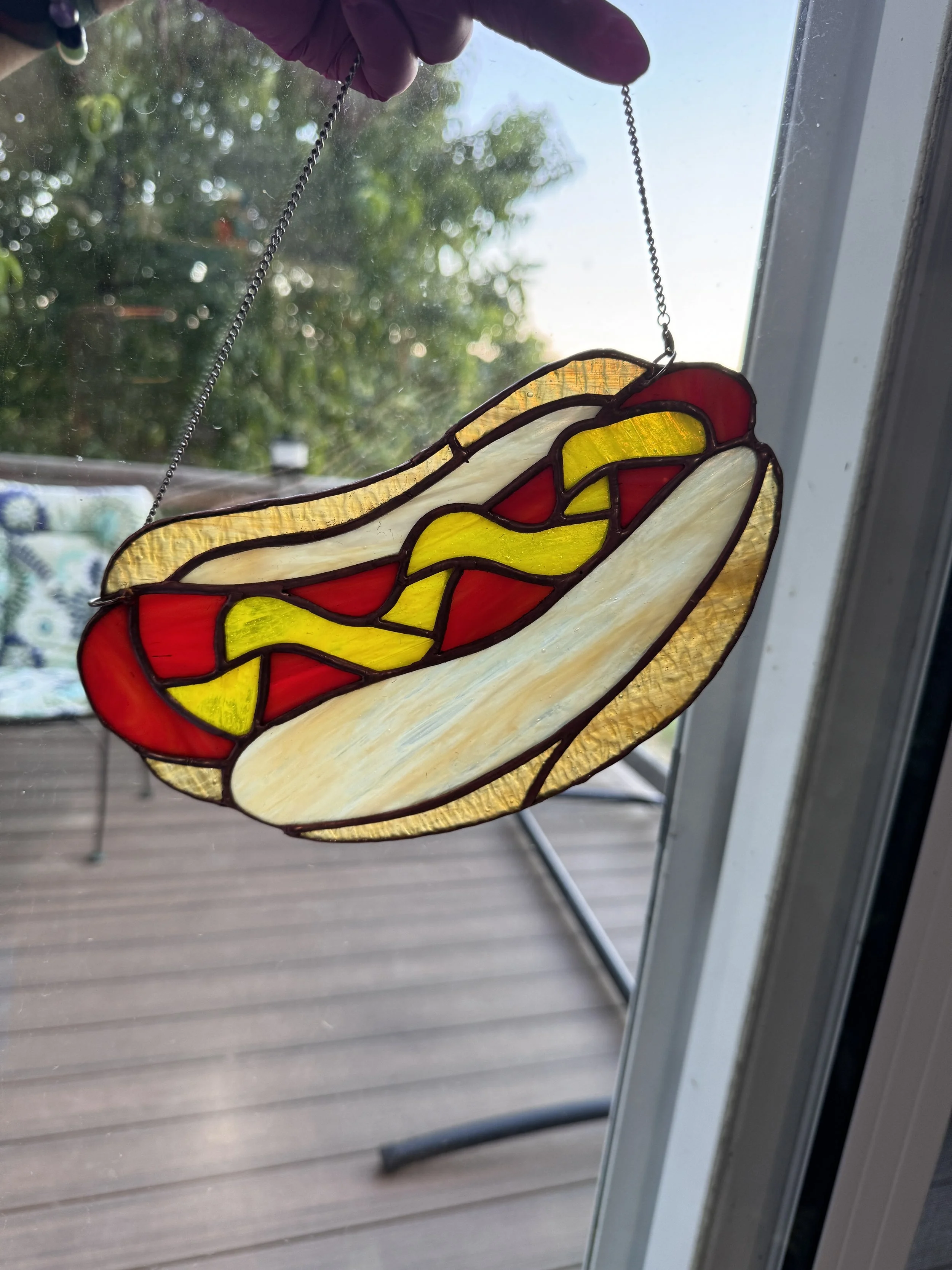 Stained glass window art depicting a hot dog with mustard and ketchup.