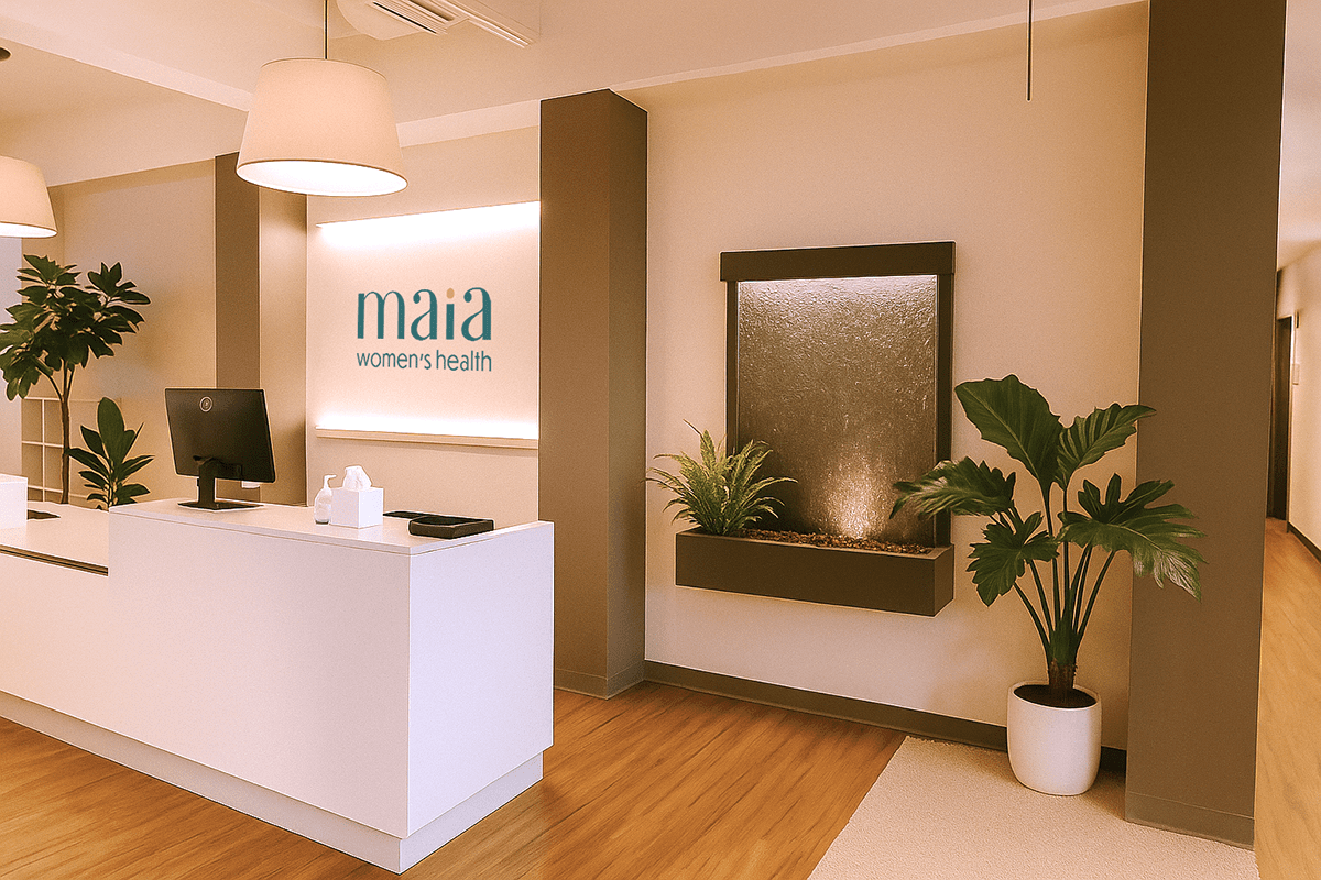 Reception desk at Maia Women's Health clinic with a computer, tissue box, and plants, featuring a water fountain on the wall and the Maia Women's Health sign.