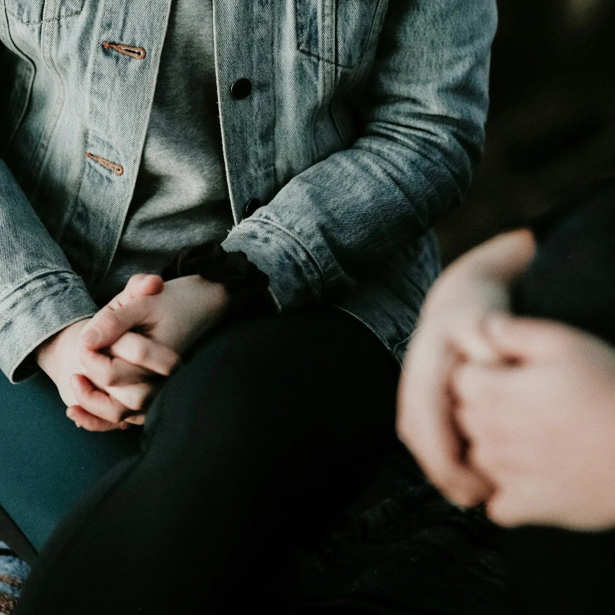 Manos entrelazadas en reposo, una persona con chaqueta de mezclilla