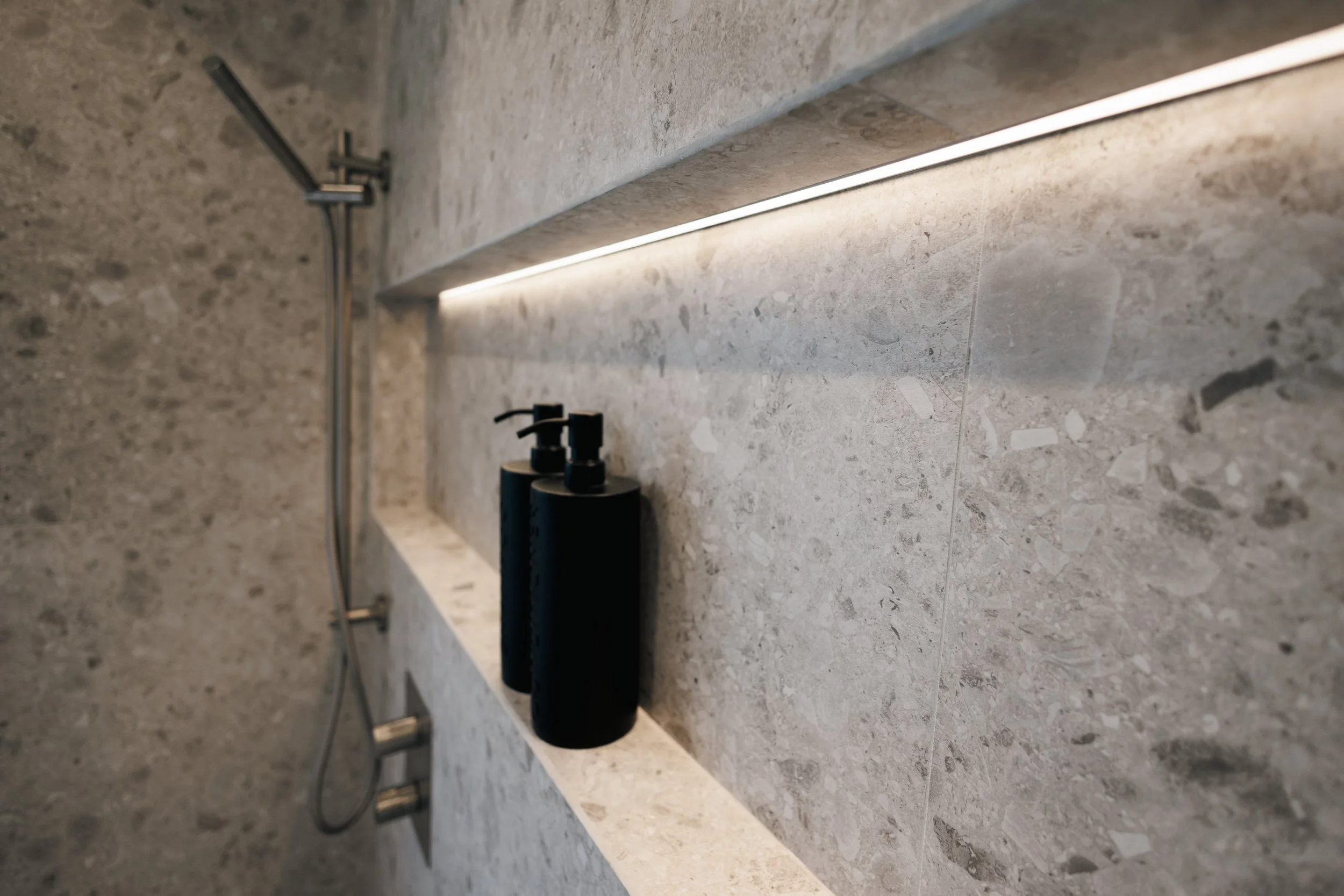 Un plan de travail en pierre avec un sèche-mains noir et des distributeurs de savon noir. La surface est en pierre avec un motif de texture gris clair.