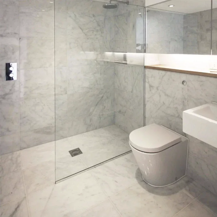 Salle de bain moderne avec mur en marbre, douche à l'italienne avec paroi en verre, toilette blanche et lavabo suspendu.