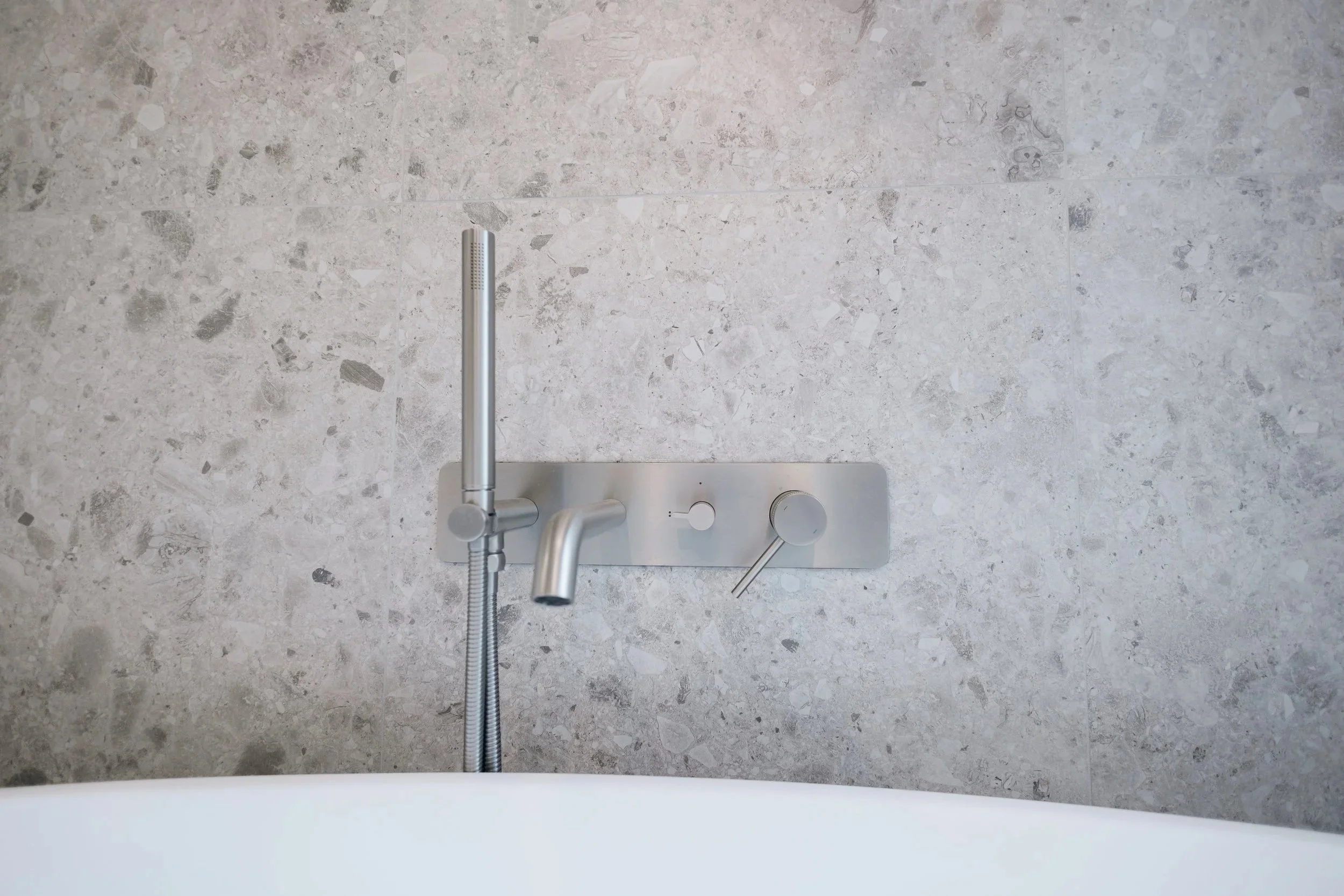 Vue du robinet d'un lavabo en métal avec bouton pour régler l'eau, fixé sur un plan en pierre claire.