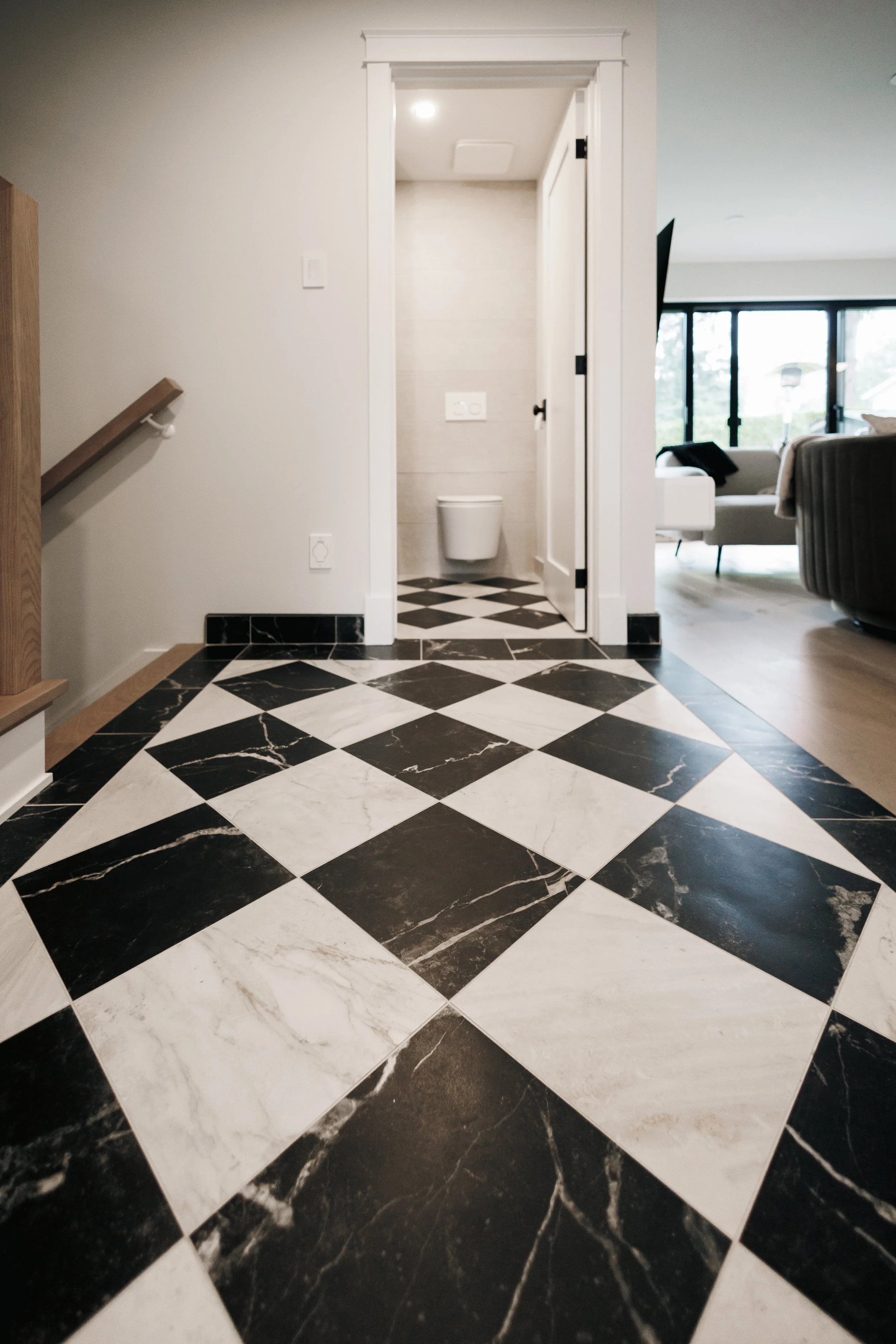 Intérieur moderne avec un sol en damier noir et blanc, un petit espace WC, et un salon lumineux avec de grandes fenêtres et des meubles contemporains.