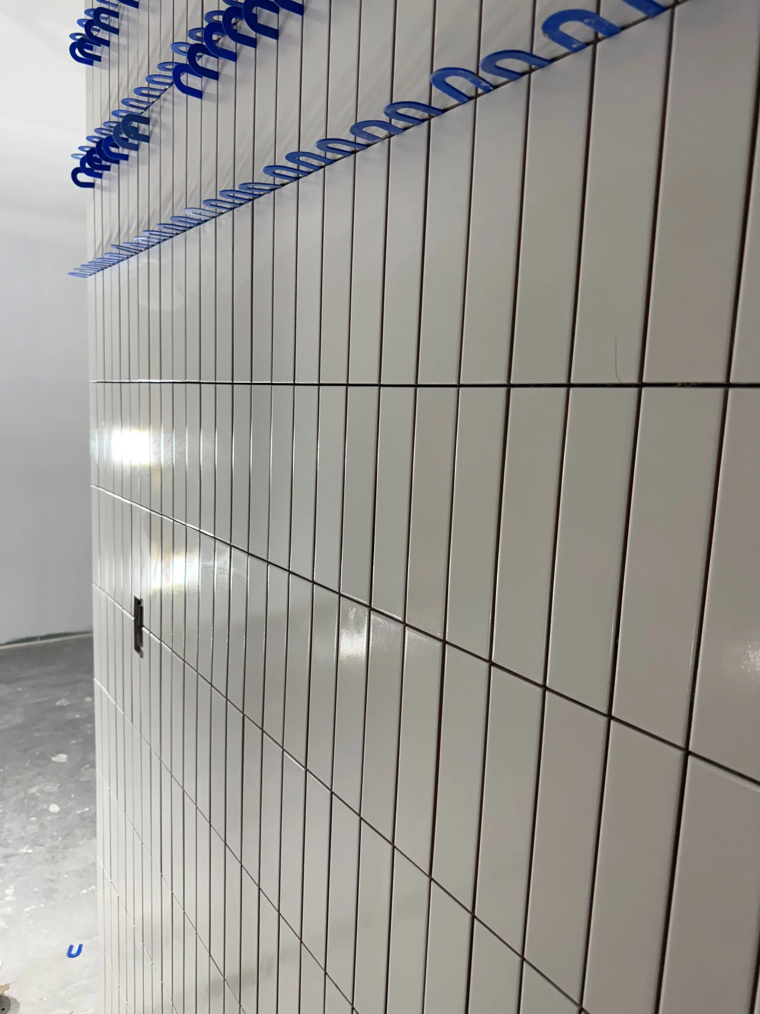 Mur en tuiles blanches avec des poignées bleues en forme de lettres« M » alignées en rangs et en colonnes.