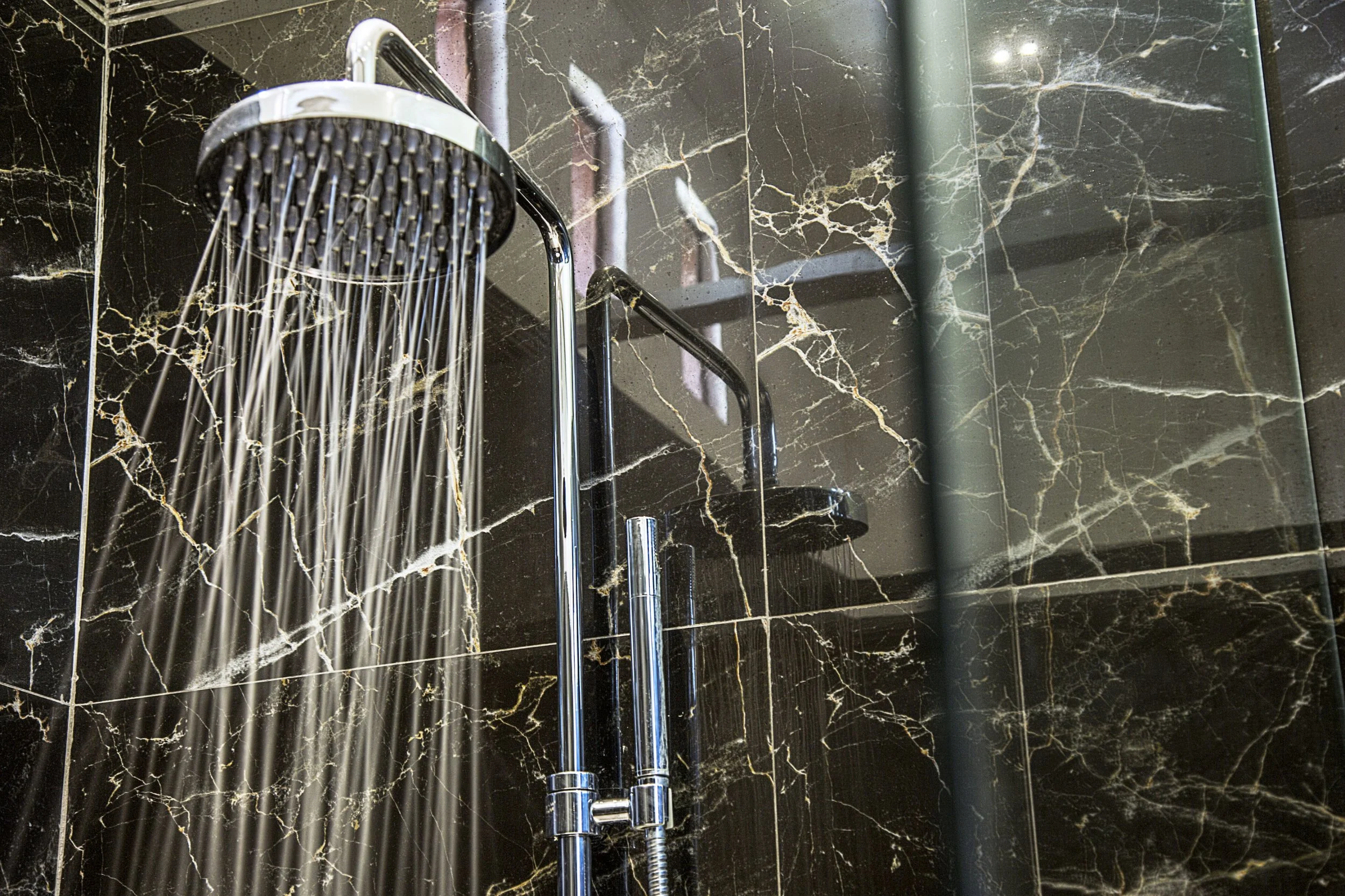 Douchette à main en métal avec de l'eau qui coule, installée sur un mur en marbre noir avec des veines blanches et dorées.