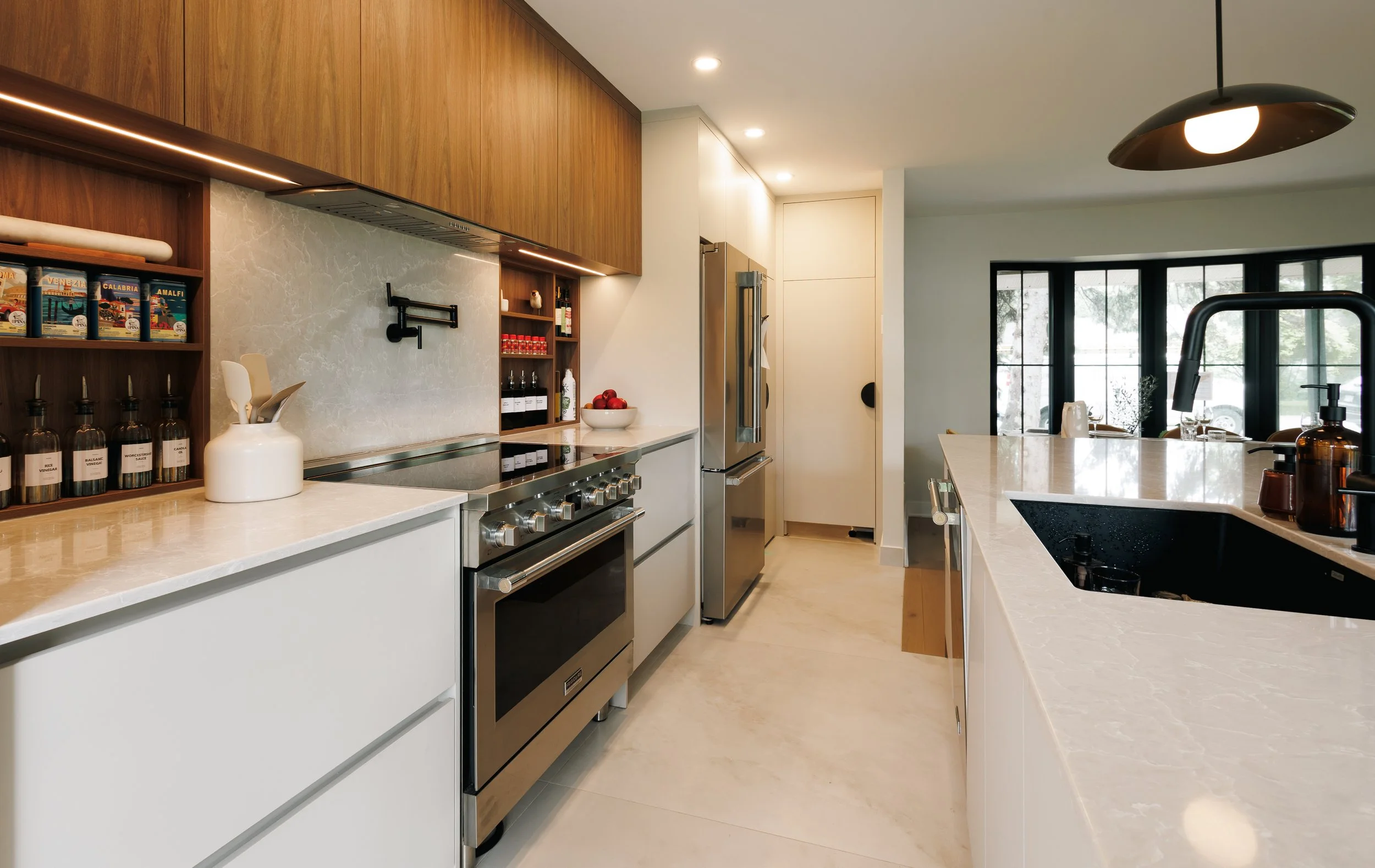 Cuisine moderne avec des armoires en bois clair, un plan de travail en marbre beige, un four à gaz en acier inoxydable, un réfrigérateur en stainless, et une grande fenêtre laissant entrer la lumière naturelle.