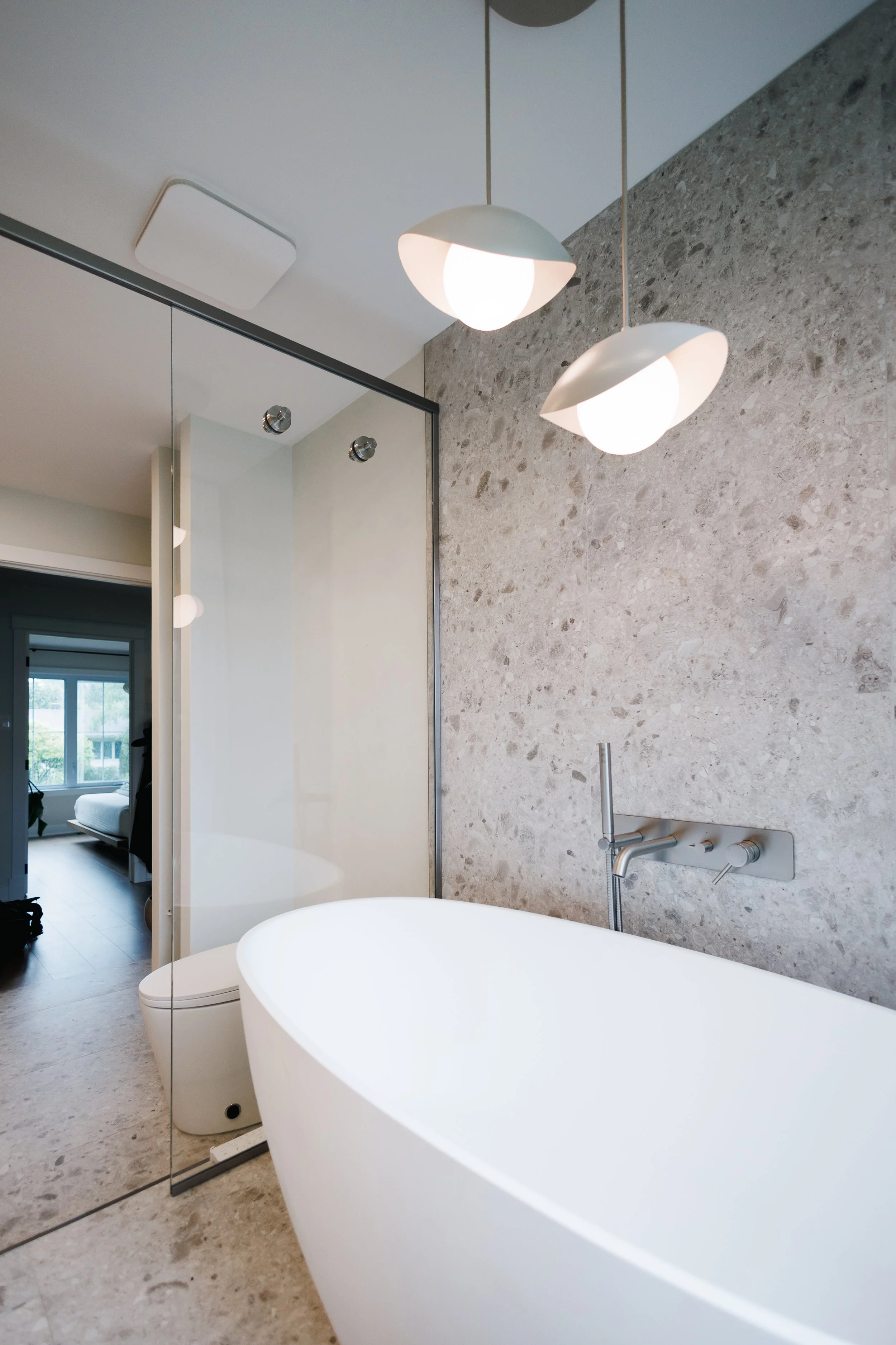 Une salle de bain moderne avec baignoire autoportante blanche, mur en pierre, robinet mural, et suspension lumineuse au plafond.