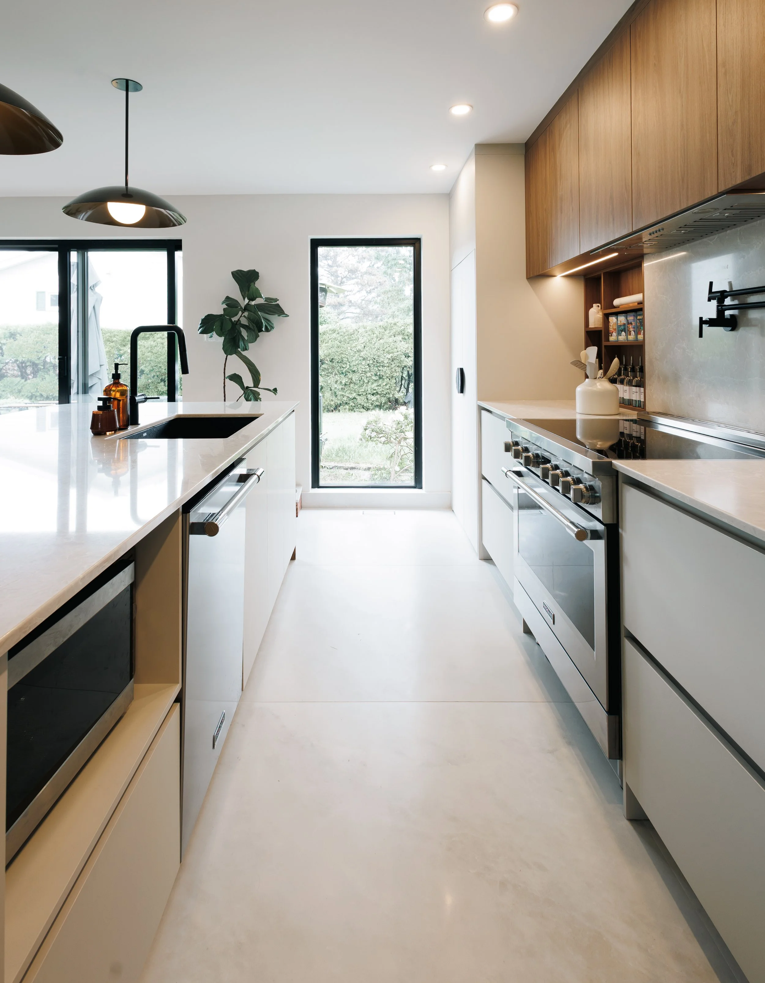 Cuisine moderne avec comptoirs en marbre, armoires en bois clair, poêle à gaz, et grande fenêtre avec vue sur un jardin.