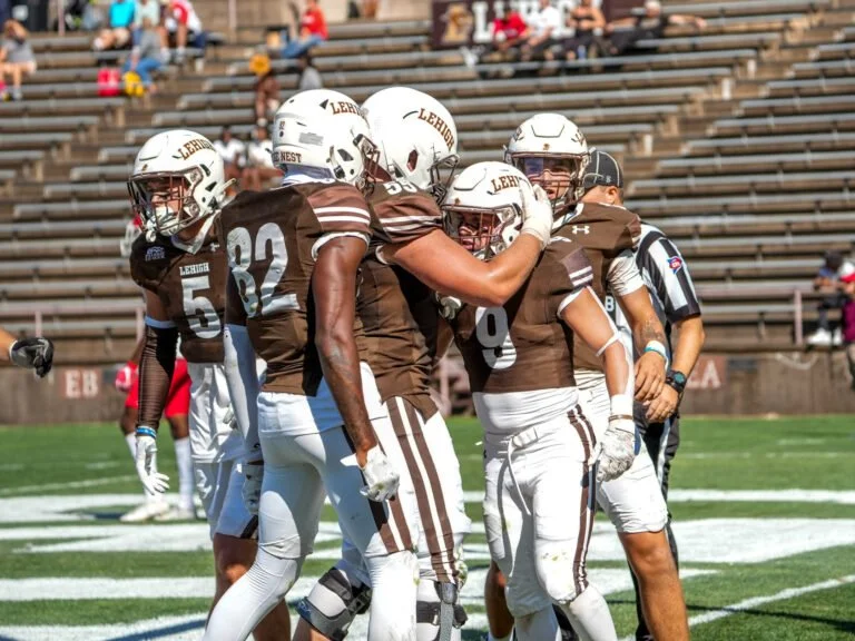 College football players in brown and white uniforms celebrate on the field as an official looks on.