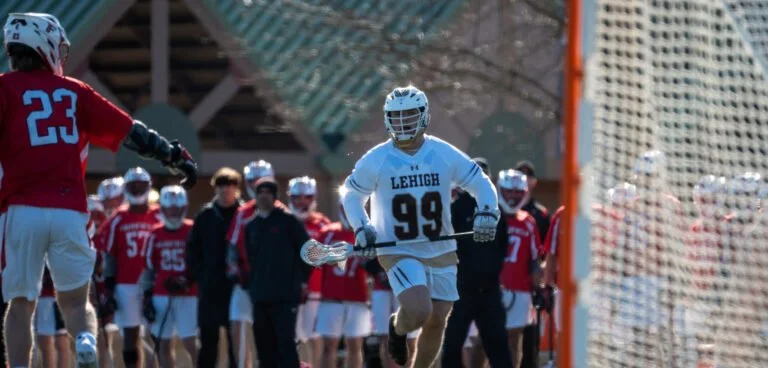Lacrosse players on the field during a game with a player wearing a white jersey with number 99 and 'Lehigh' written on it.