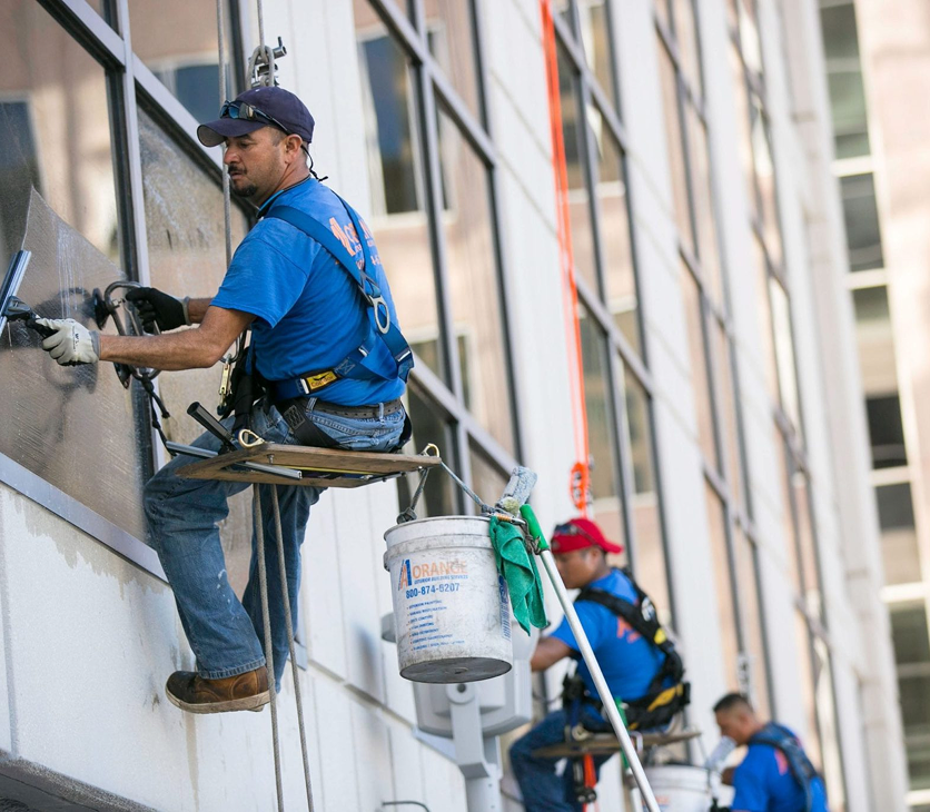 Construction workers installing or repairing windows on a tall building's exterior, using harnesses and scaffolding.