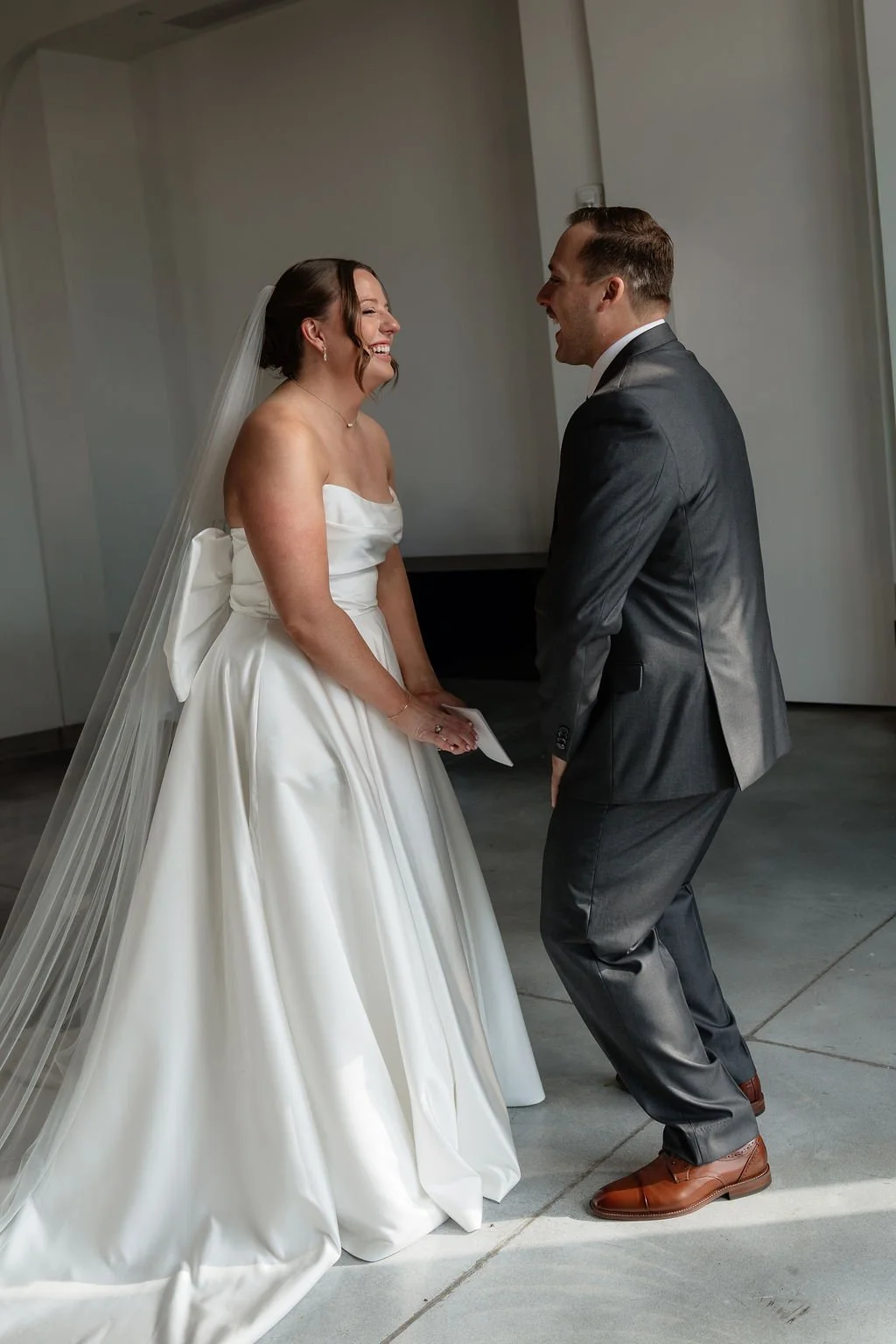 A bride and groom laughing and holding hands during their wedding ceremony indoors.