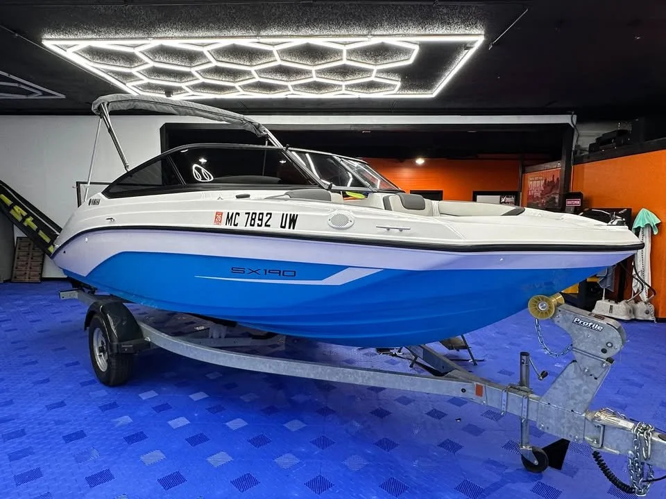 A blue and white speedboat on a trailer inside a showroom with a black ceiling and hexagonal LED lights.