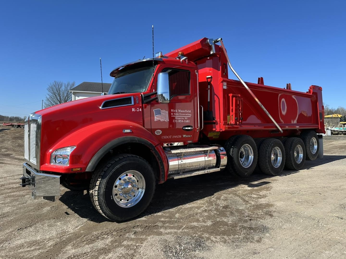 Red fire truck with multiple axles parked on a dirt lot under a clear blue sky.