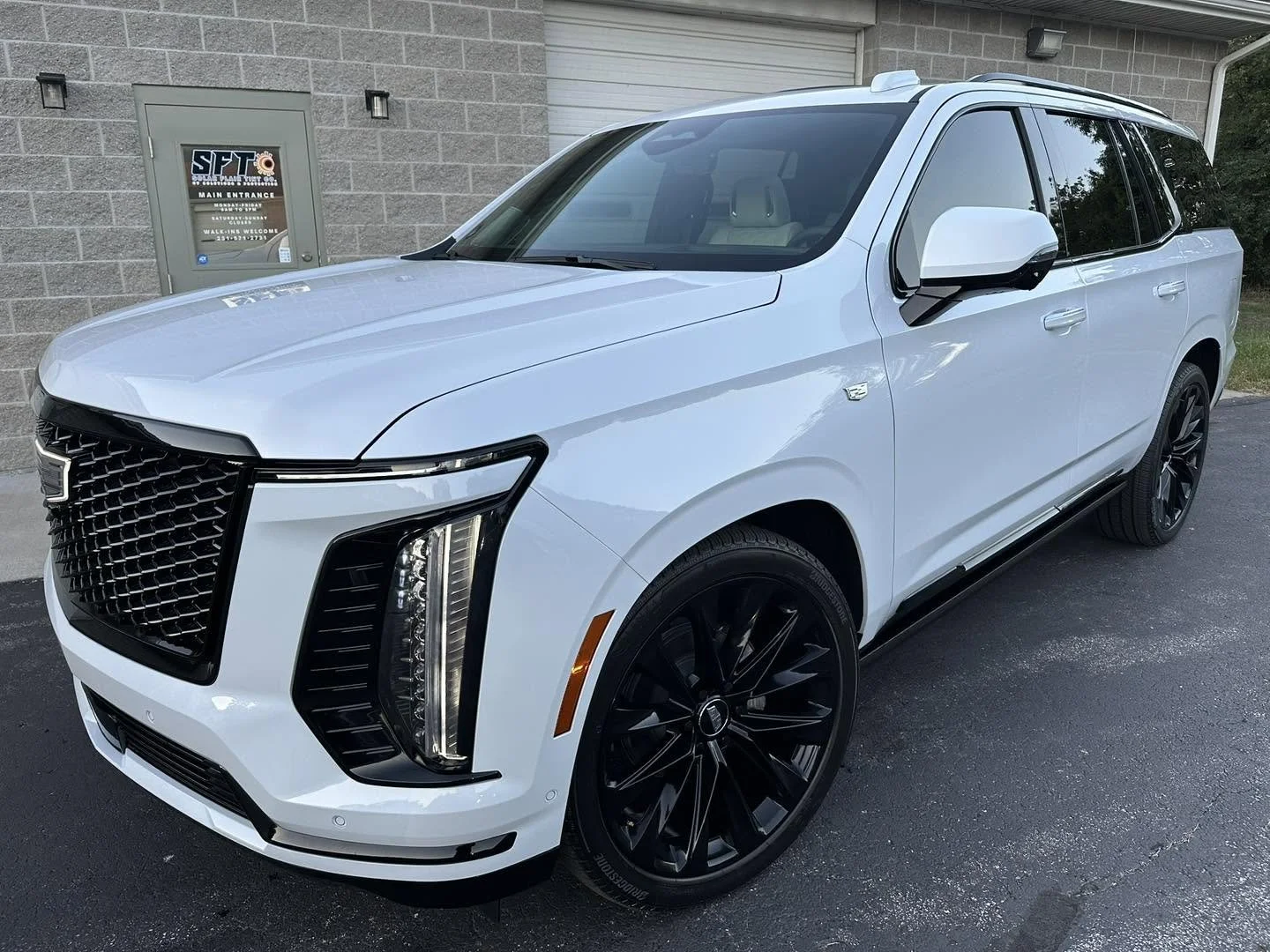 White luxury SUV parked outside a building with a gray brick wall, featuring dark tinted windows, black rims, and a distinctive front grille.