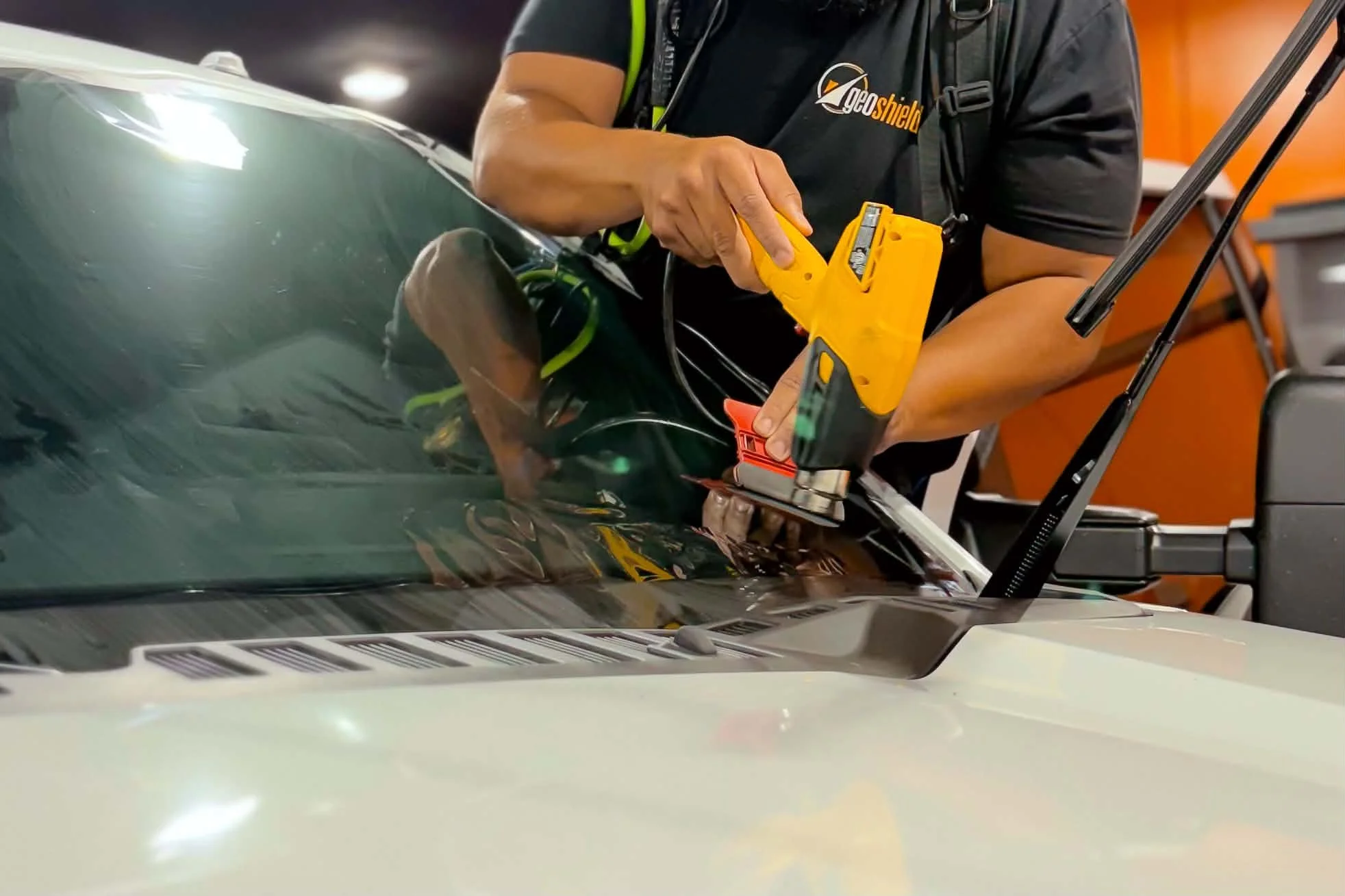 Person in a black shirt applying a protective film to a car windshield with a yellow tool.