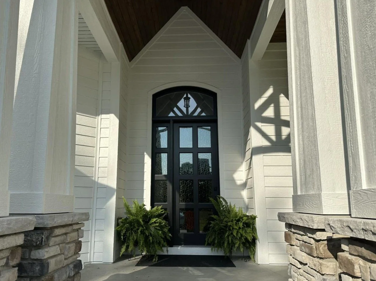 Front entrance with black door, white siding, stone pillars, and potted plants.
