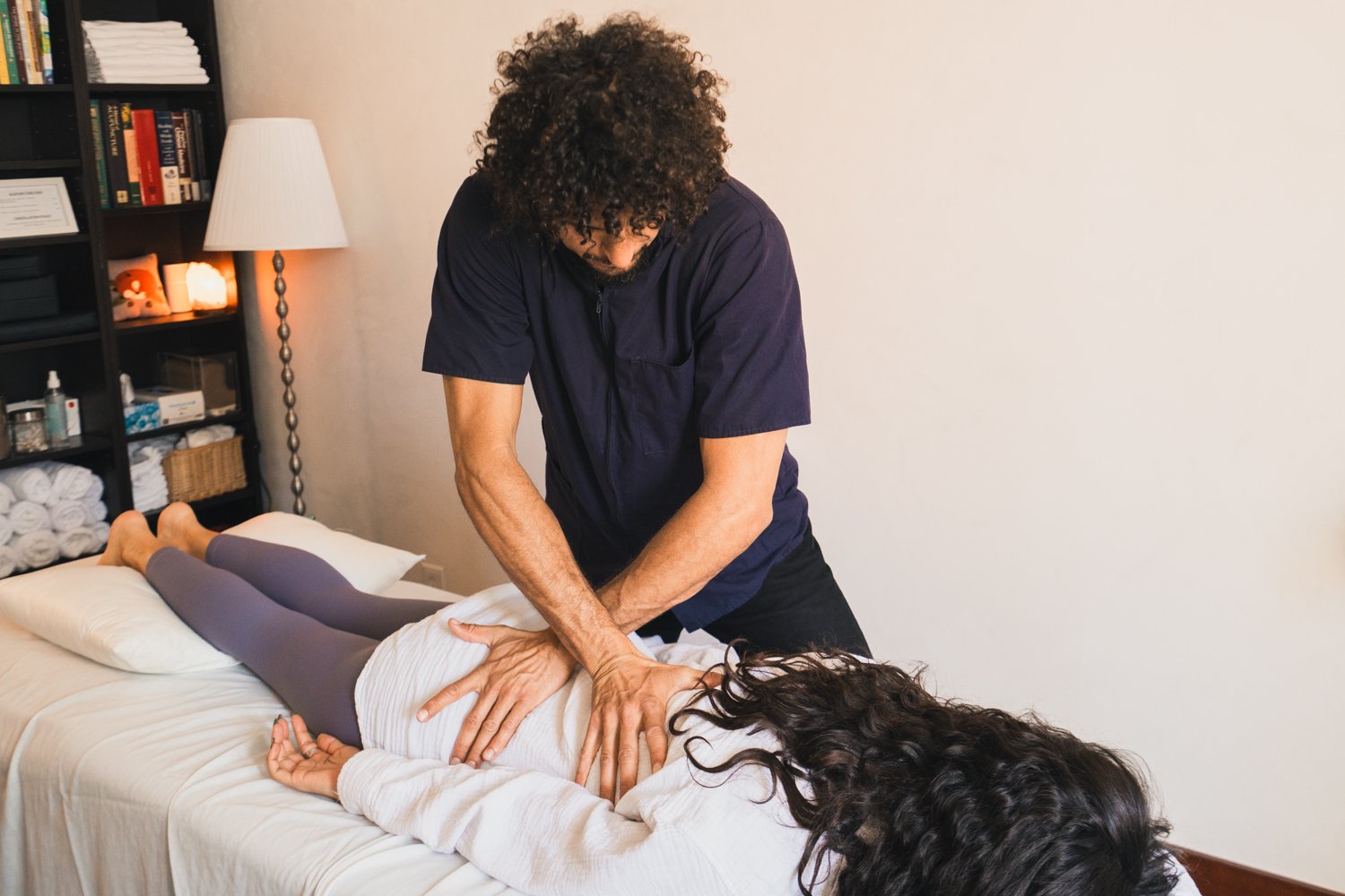 A chiropractor adjusting a woman's back during a session in a therapy room.