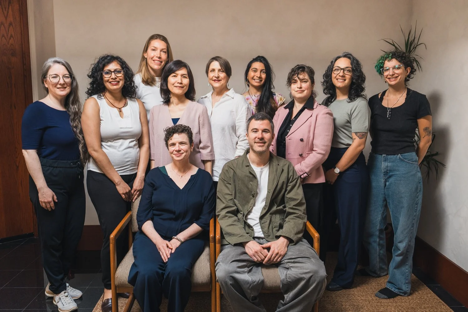 Group of fifteen diverse women and two men posing for a photo in an indoor setting.