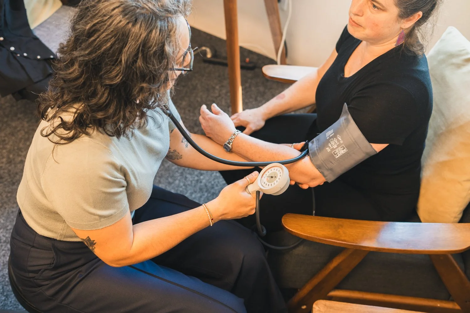 A nurse measuring a woman's blood pressure using a sphygmomanometer in a healthcare setting.