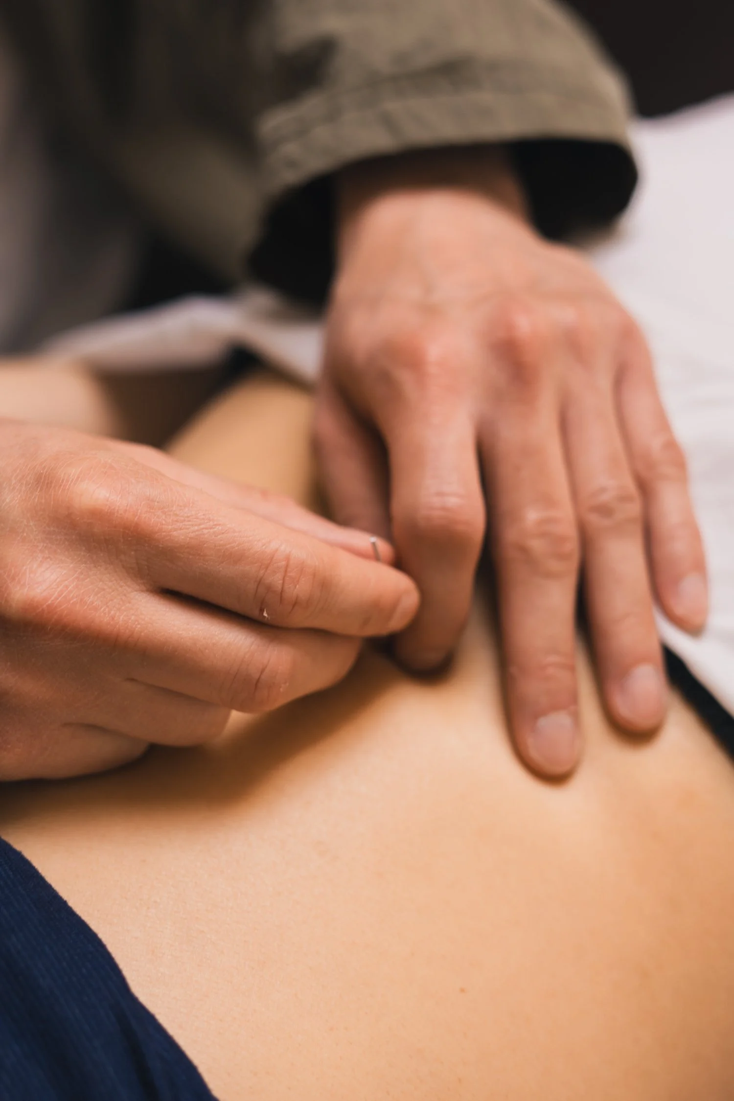 Close-up of a hand pressing on a person's back during massage, with the person's shoulder and part of their arm visible.