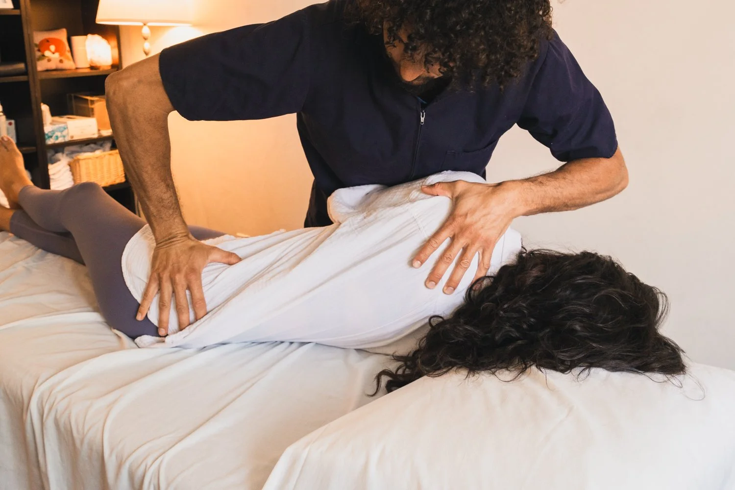 Chiropractor performing a spinal adjustment on a woman lying face down on a bed.