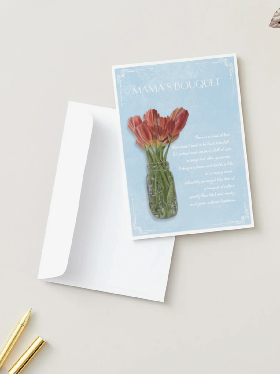 A greeting card with a photo of red tulips in a glass jar and the text 'Mama's Bouquet' on a light blue background, placed on an open white envelope, with a gold pen nearby.
