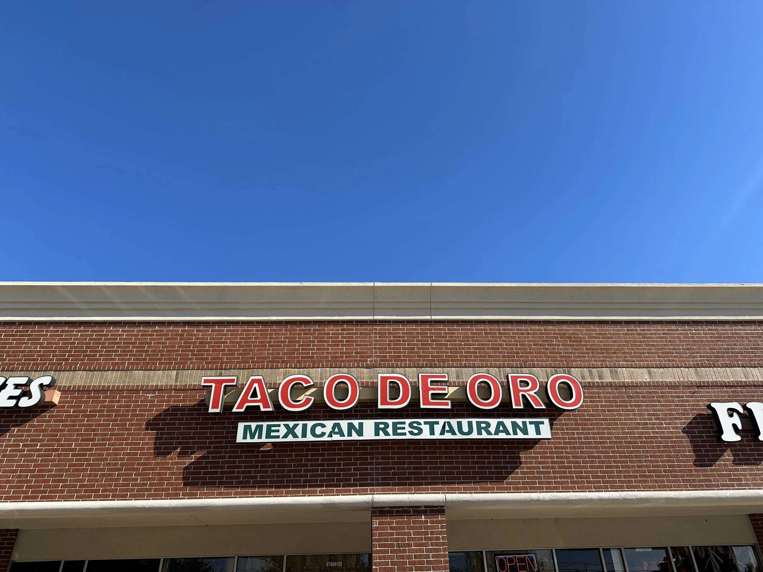 Sign for Taco De Oro Mexican Restaurant on a brick building under a clear blue sky.