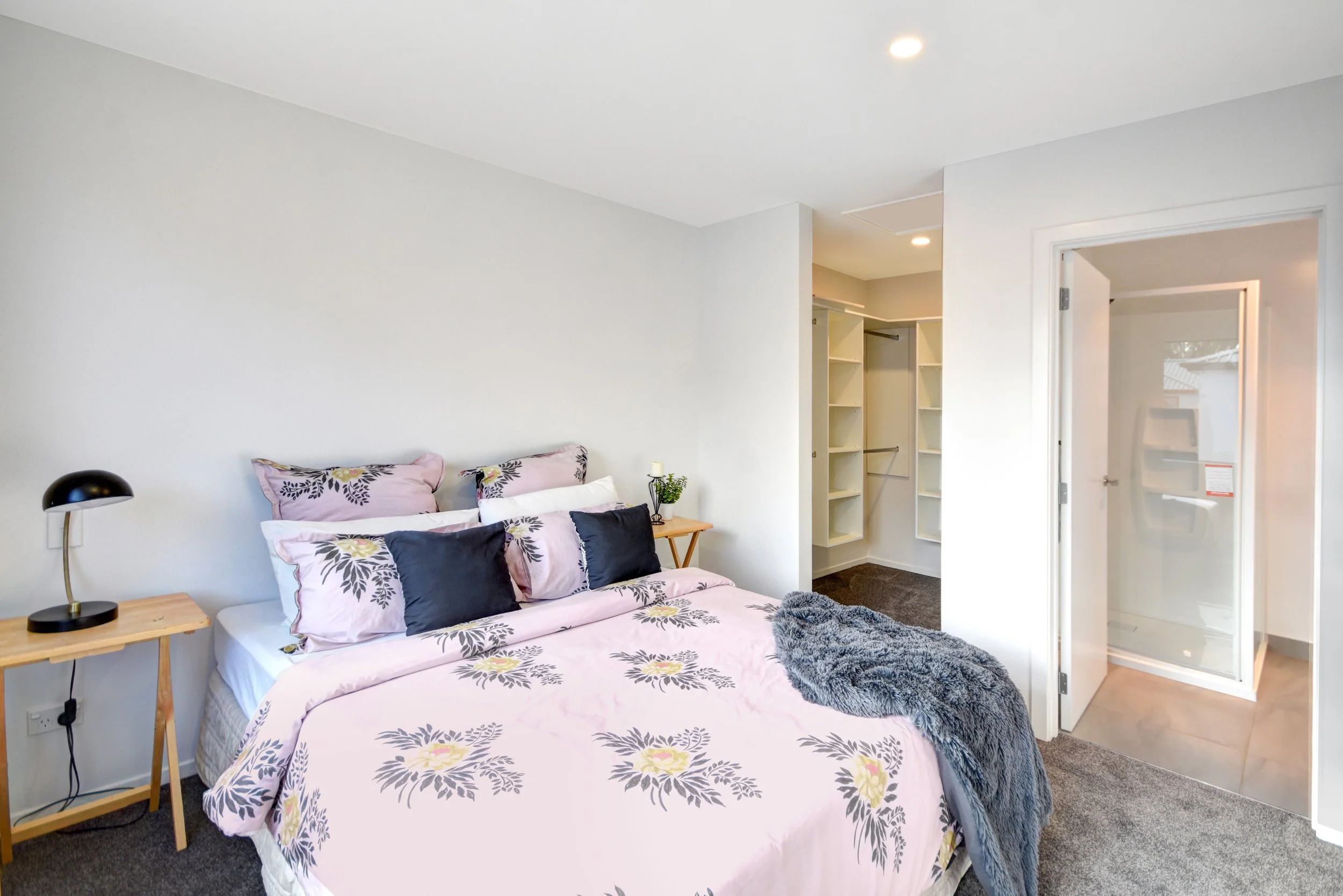 Bedroom with bed, bedside table, lamps, open closet, and walk-in shower.