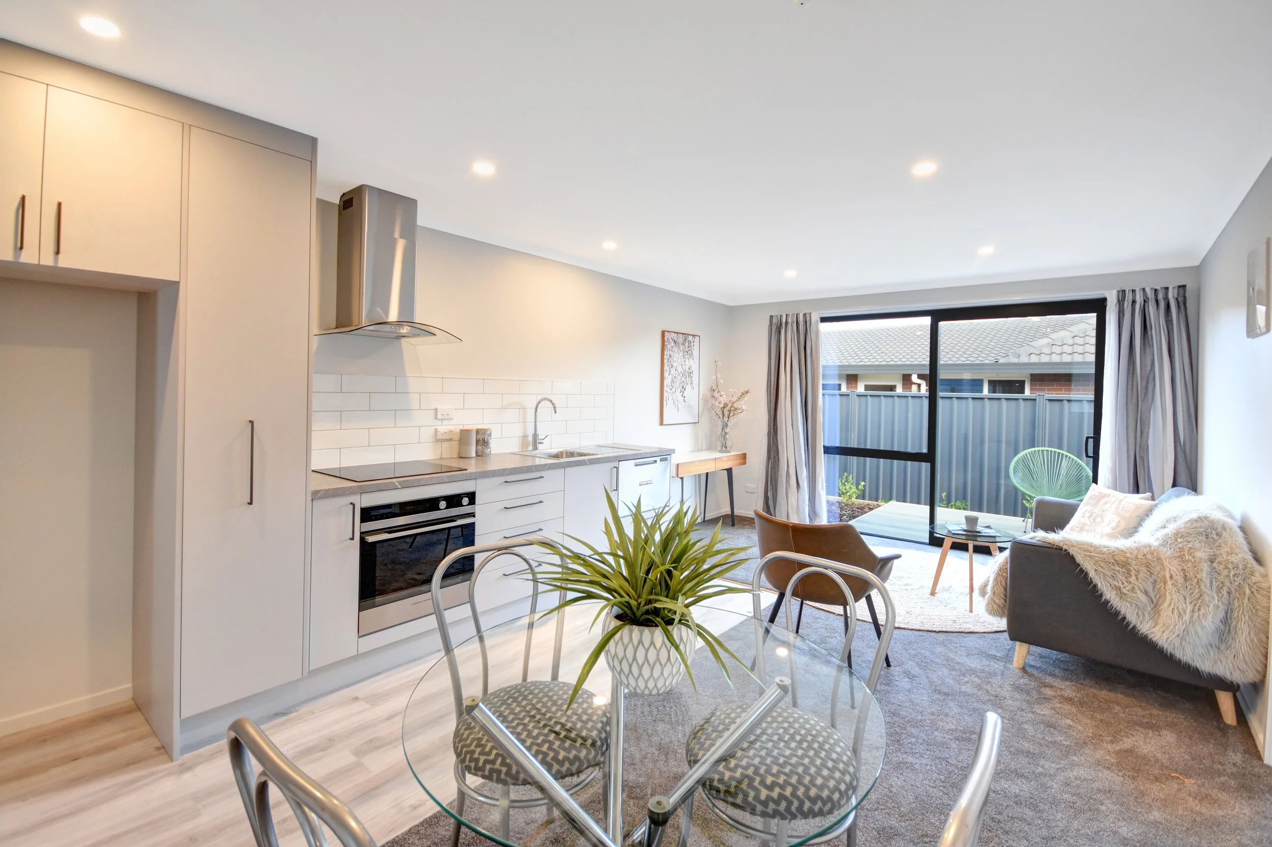 Open-plan living room and kitchen with dining table, chairs, sofa, armchair, and large sliding glass door leading to outdoor patio