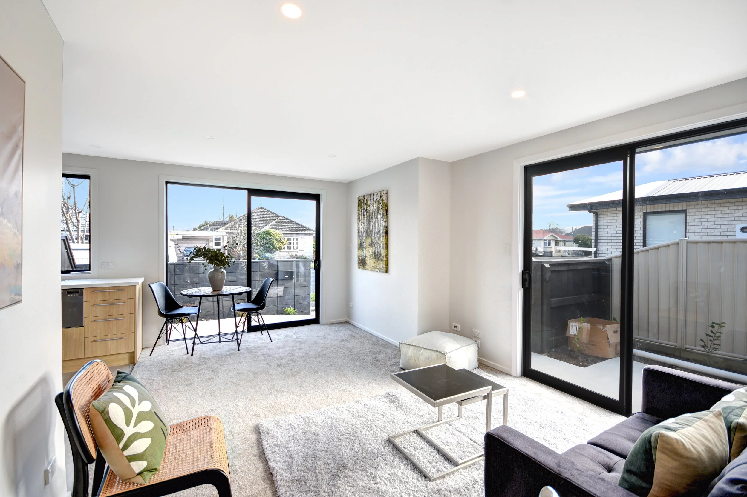 Living room with large sliding glass doors, a small round table with chairs, a sofa with pillows, and a side table.