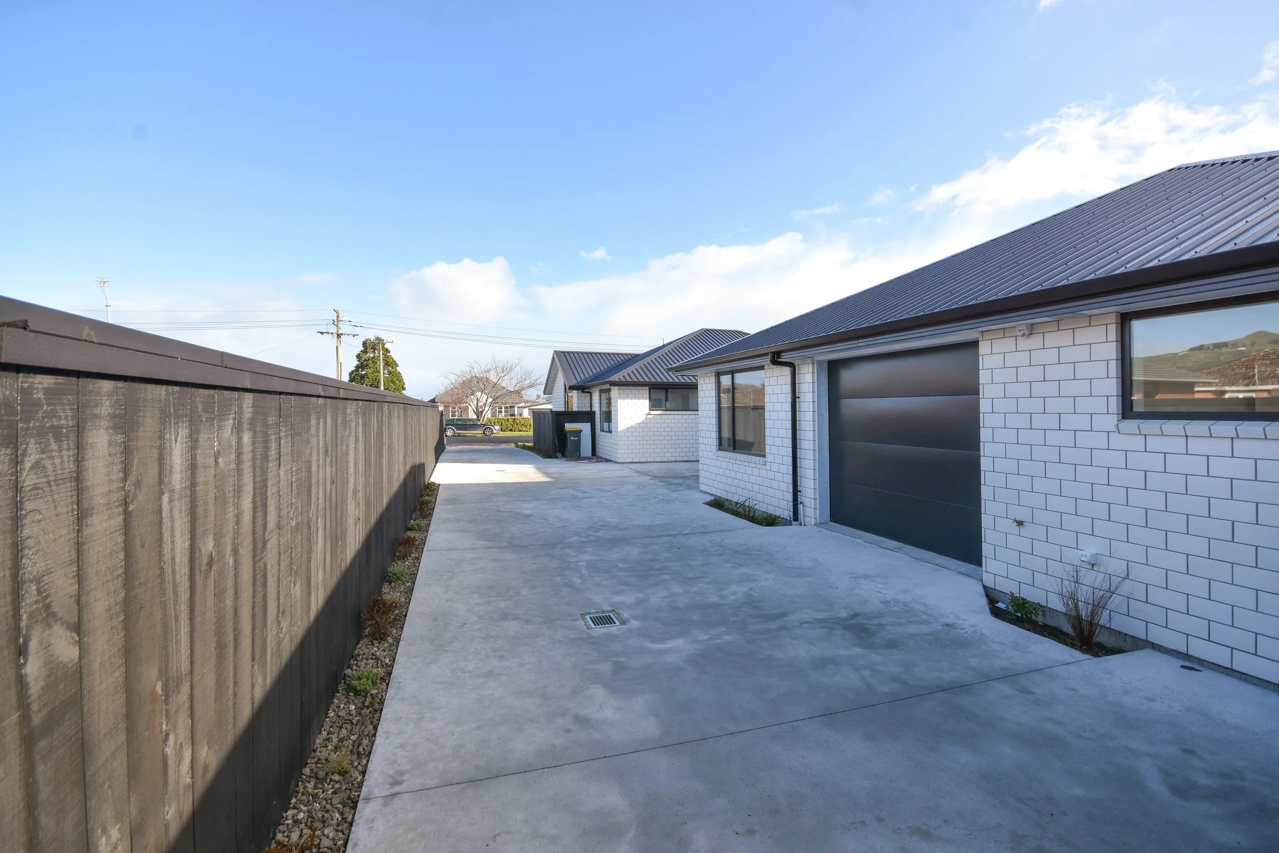 Modern white brick house with dark gray garage door, concrete driveway, black fence, and blue sky with clouds.