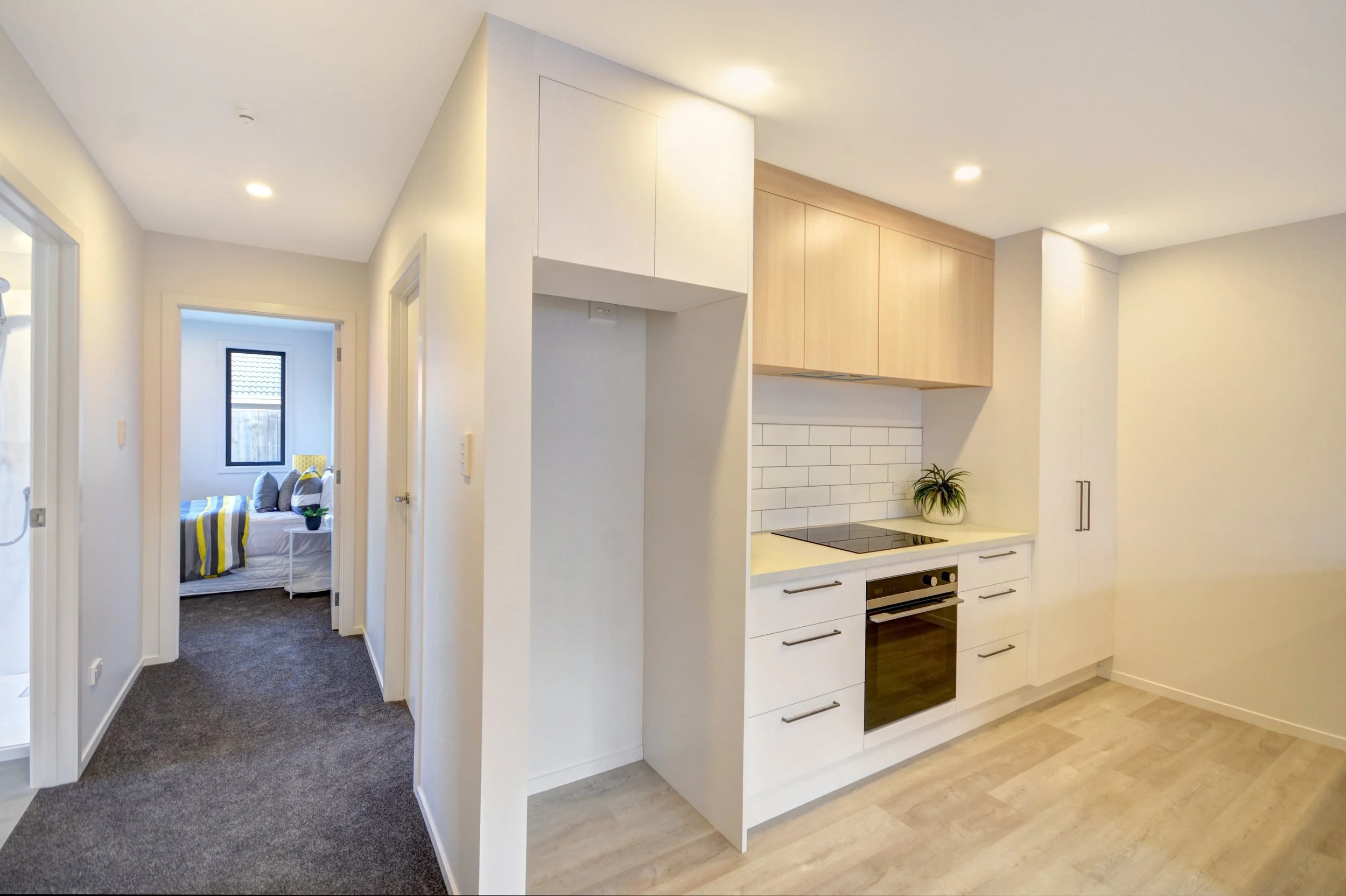 Modern kitchen with white cabinets, wooden upper cabinets, white subway tile backsplash, black stovetop, oven, and a potted plant on the counter.