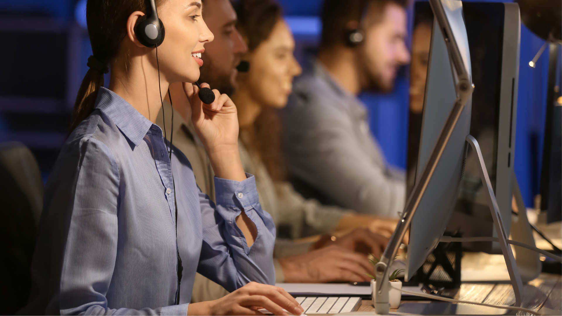 A group of people working at computer stations, wearing headsets, in a modern office environment.
