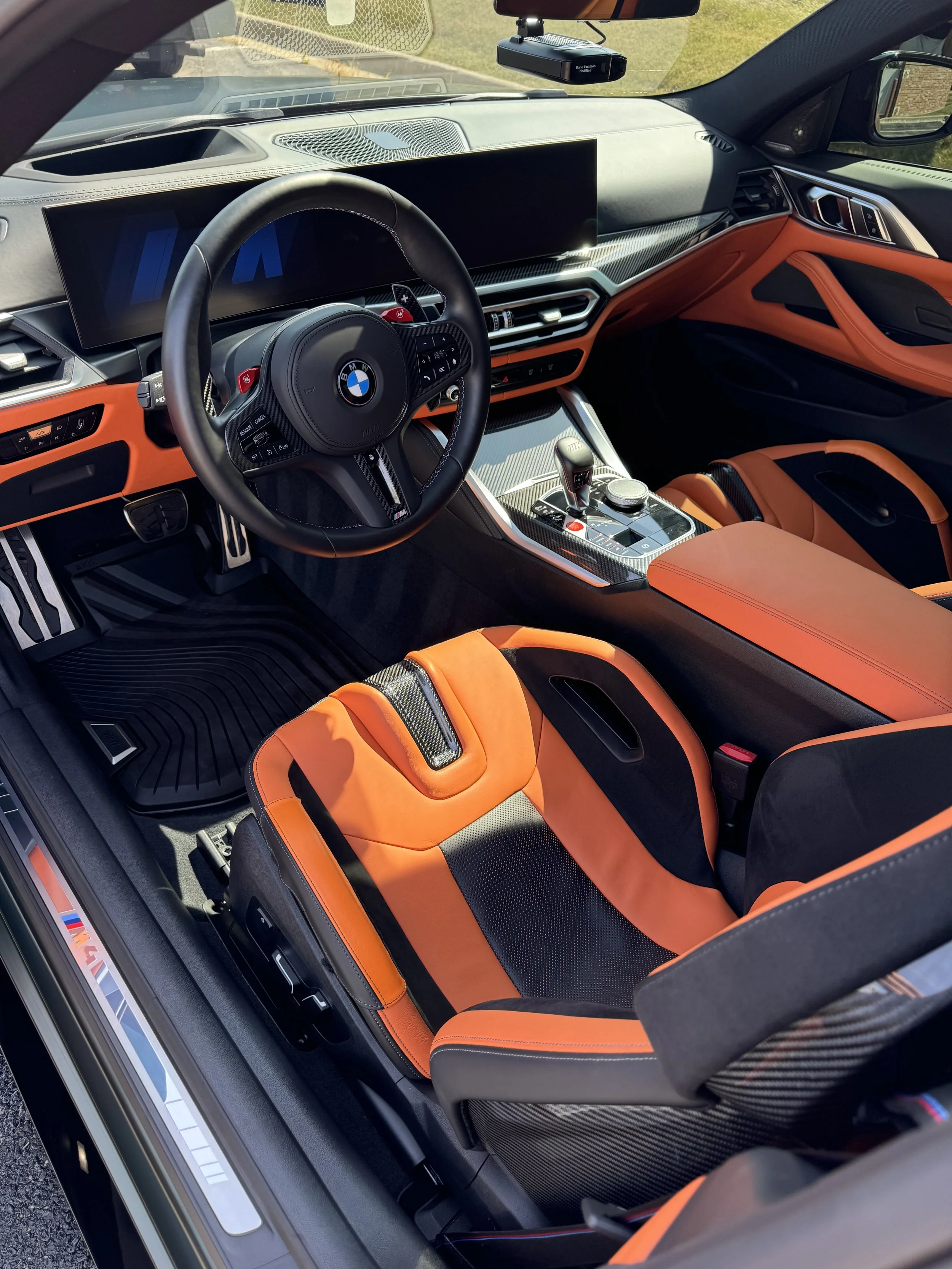 Interior of a BMW car with black and orange racing seats, a digital dashboard, and a modern center console with gear shifter and controls.