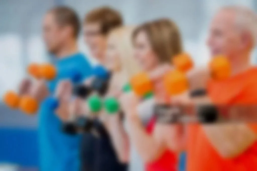 Blurred image of four people holding dumbbells during a workout.
