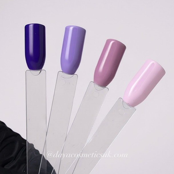 Four different shades of nail polish bottles in blue, purple, mauve, and light pink, each placed on clear angled stands.