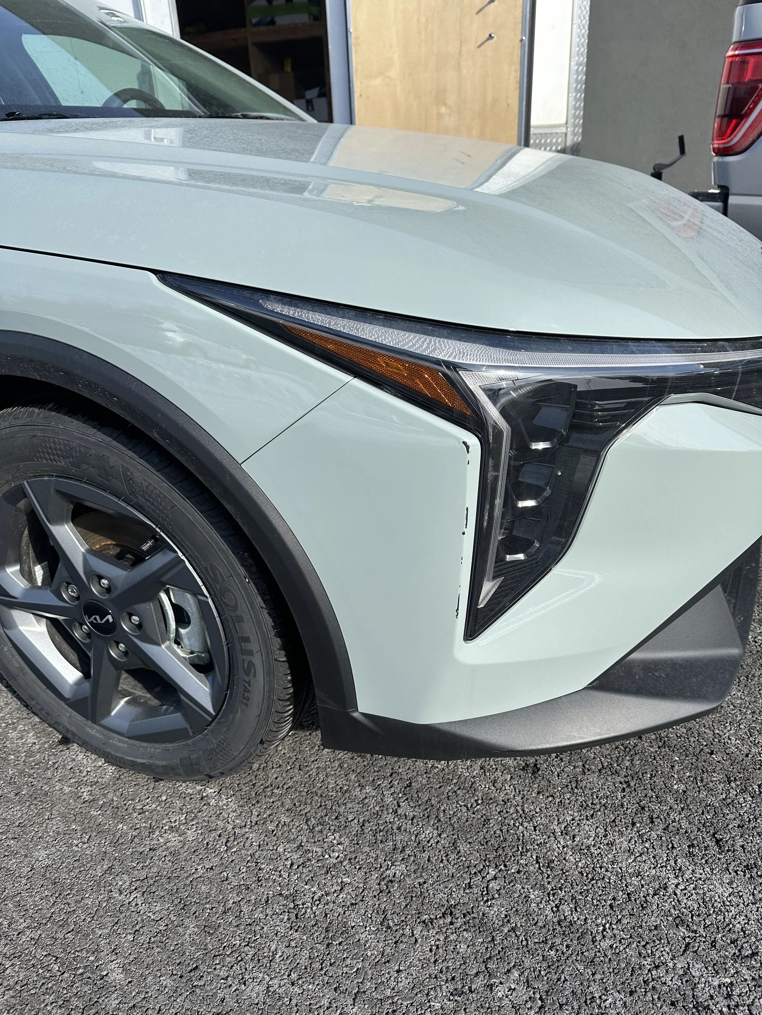 Front left side of a white Kia electric vehicle with modern angular headlight design and a black front bumper, parked on an asphalt surface.