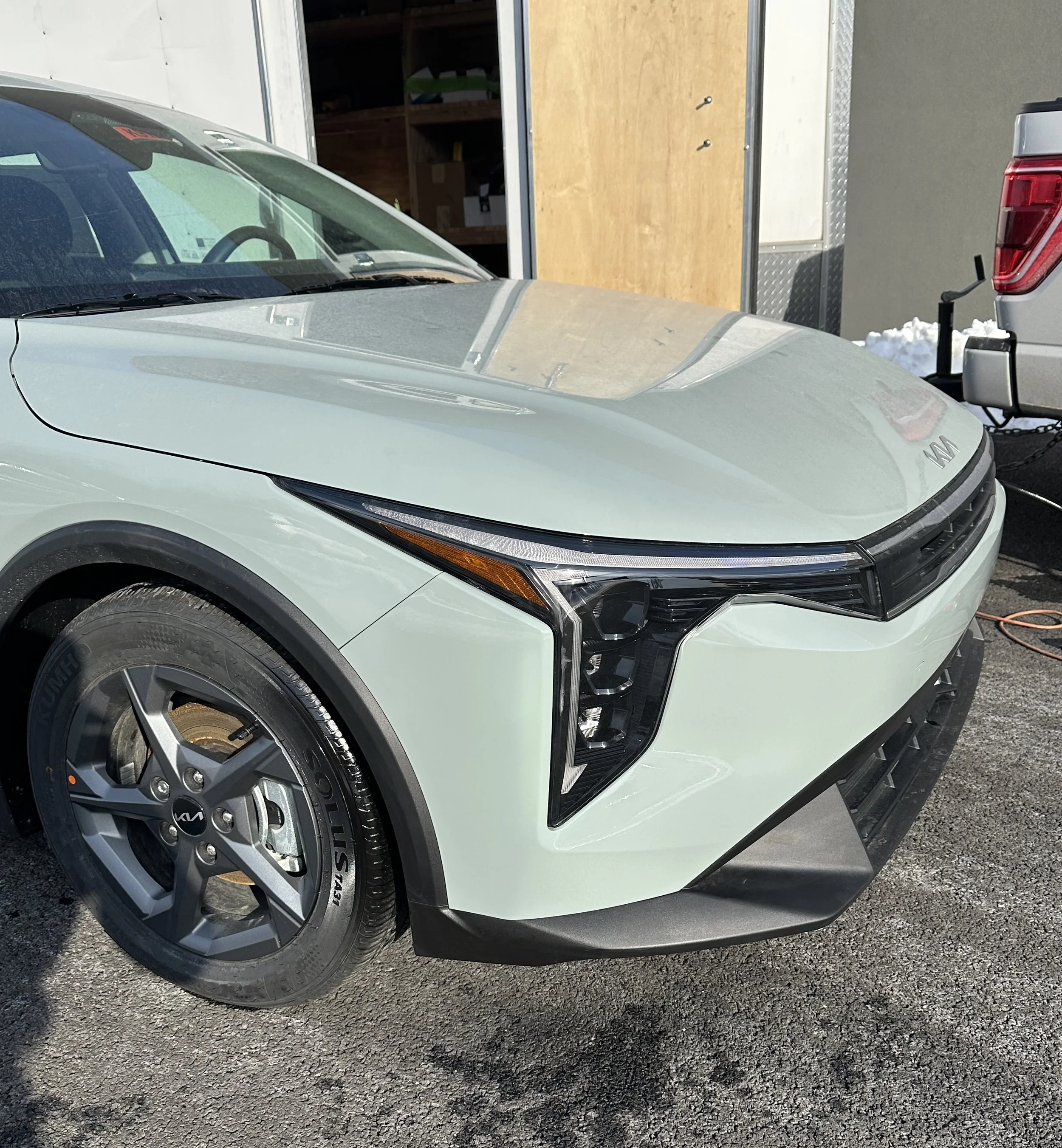 Front view of a light green electric vehicle with black accents, parked outside near a building, connected to a trailer.