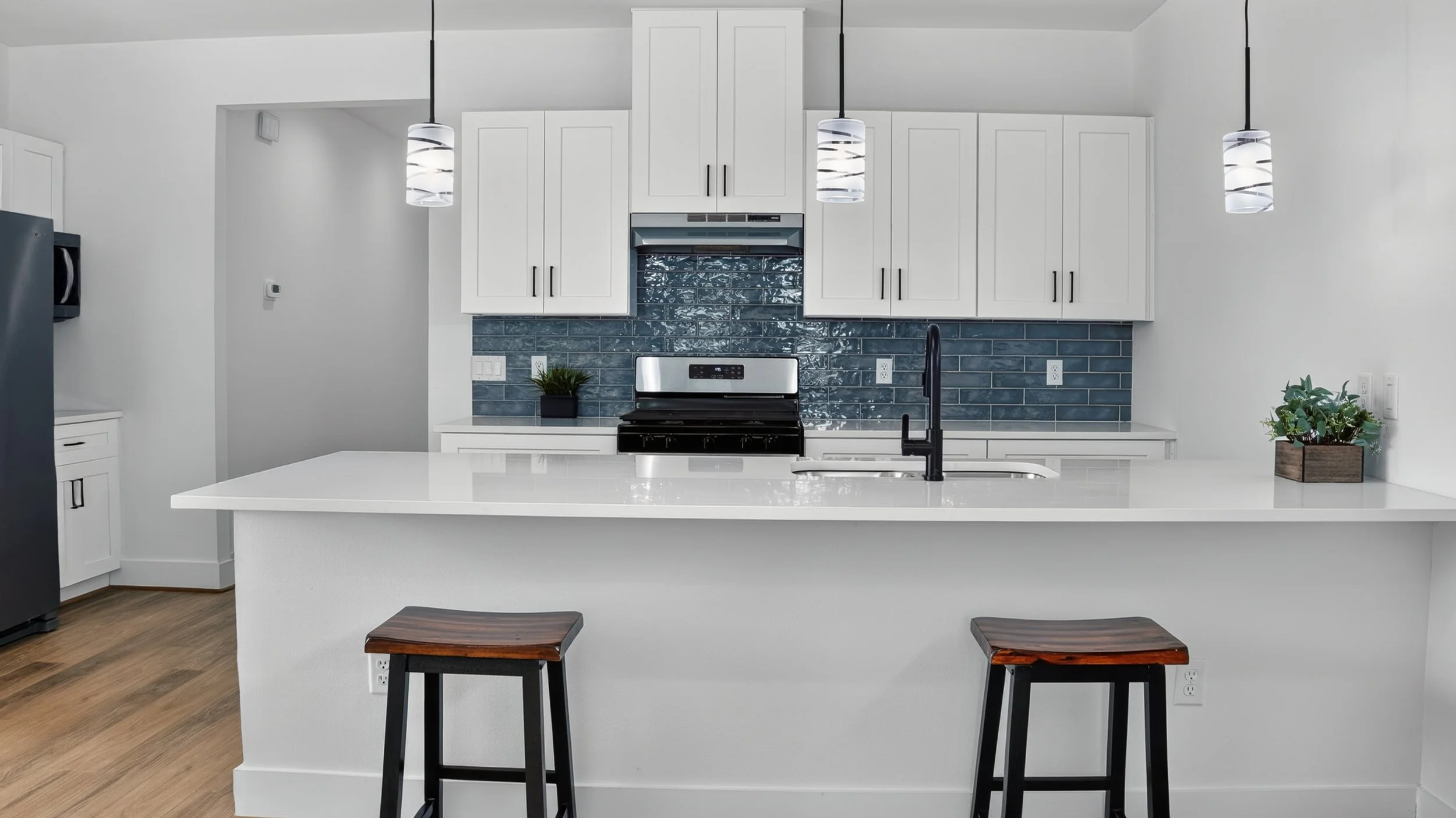 Open kitchen with white cabinets, blue tile backsplash, and pendant lights close up