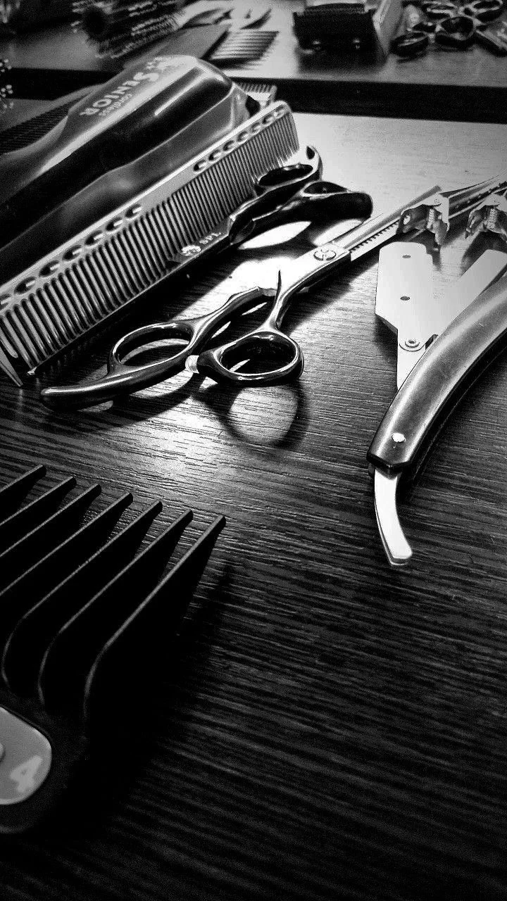 Barber tools on a wooden surface including scissors, hair clippers, and a razor.