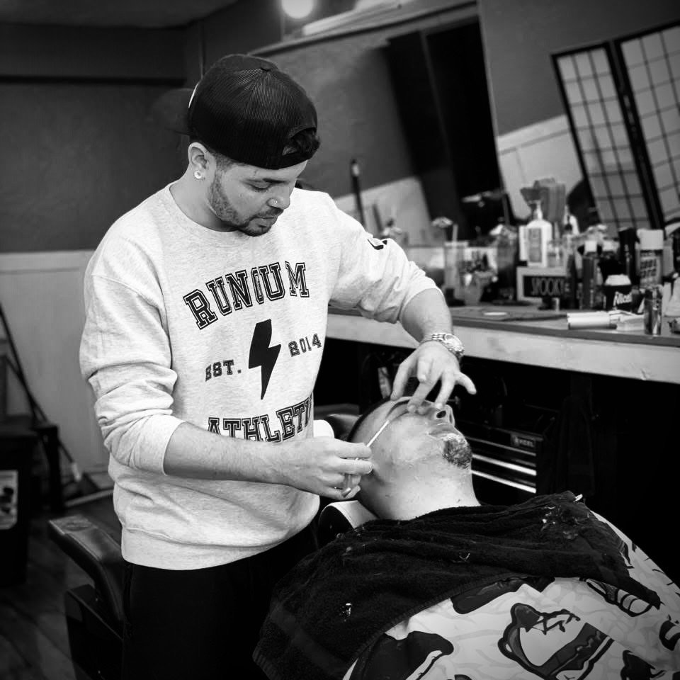 A man in a baseball cap and sweatshirt providing dental care to a patient lying in a dental chair, in a dental office.