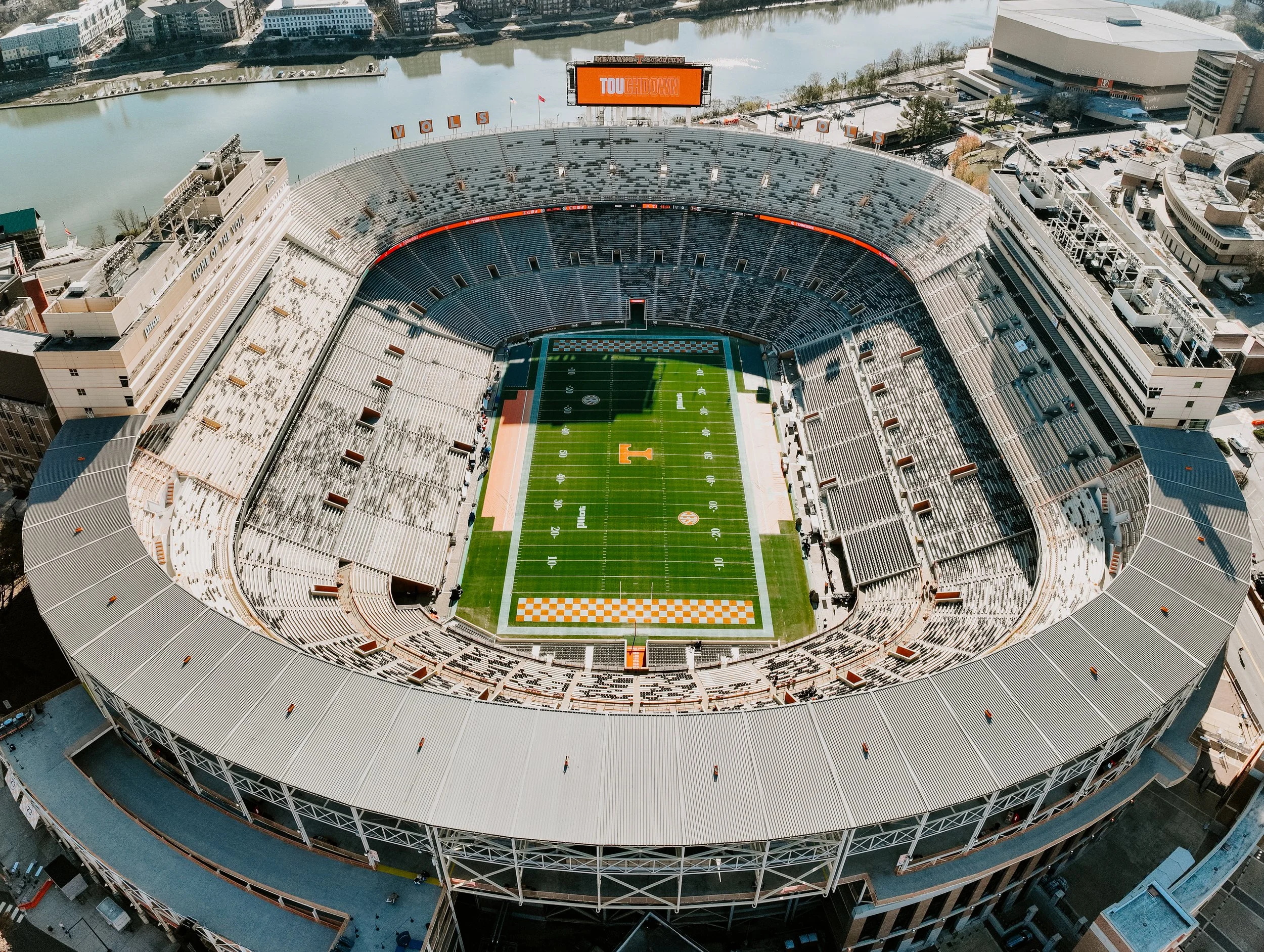 Aerial view of Neyland Stadium in Knoxville, Tennessee, with a football field inside and a large digital scoreboard displaying the words "TOUCHDOWN".