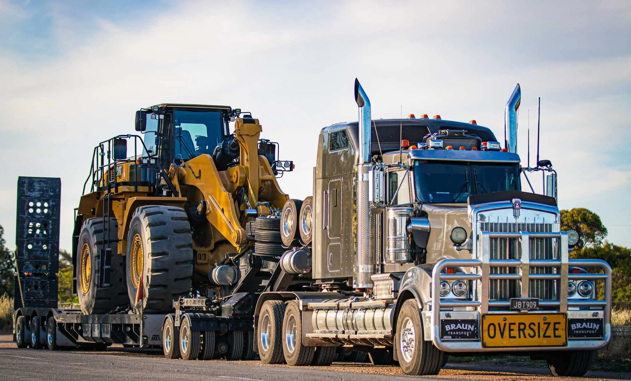 Oversized truck transporting a yellow construction loader on a flatbed trailer